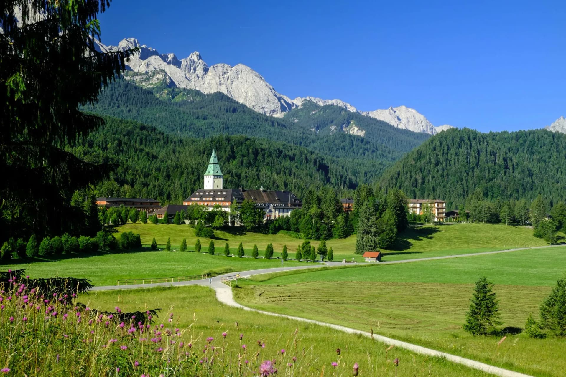 Hotel Elmau nestled in a green valley with towering, rocky mountains behind.