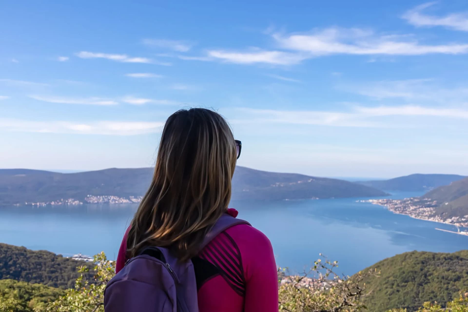 Woman with scenic view from mountain summit of Vrmac Sveti Ilija on Kotor bay in summer, Adriatic Mediterranean Sea, Montenegro, Balkans, Europe. Fjord winding along coastal towns. Hiking Dinaric Alps