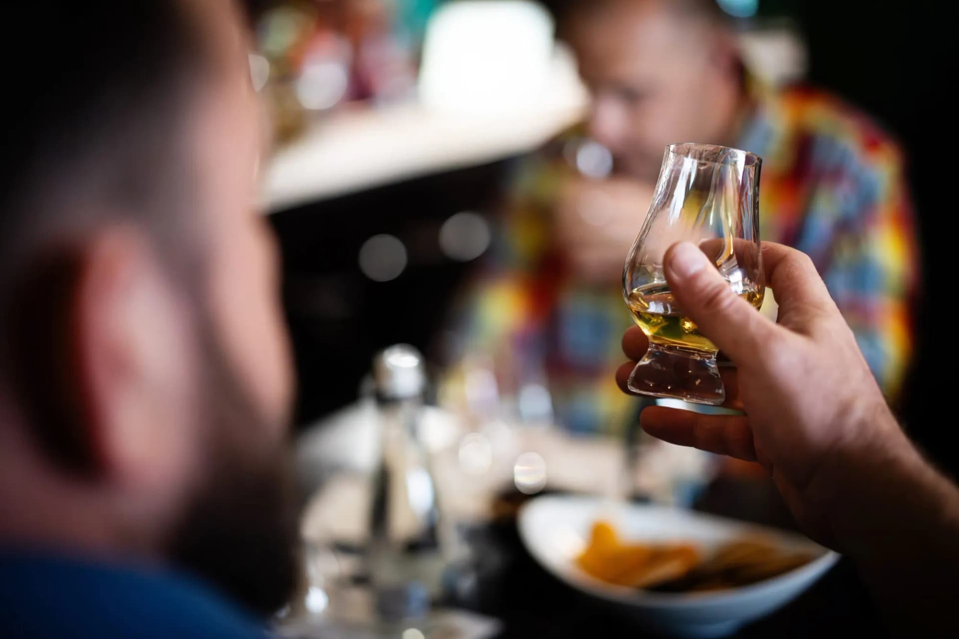 Hand holding a tulip-shaped glass with amber liquor during a tasting event indoors