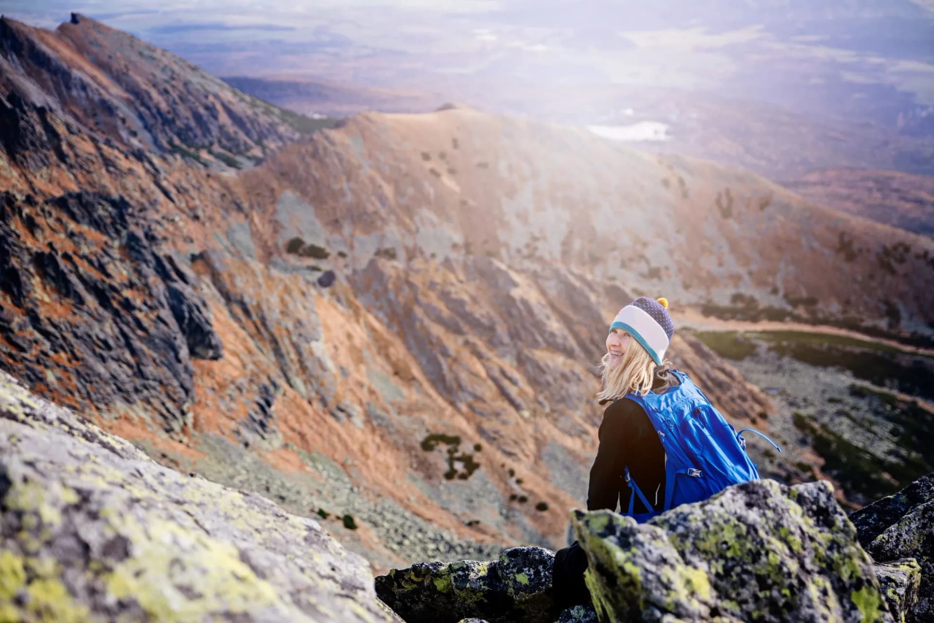 Beautiful blonde woman enjoys the moment while hiking in the Slovak Tatra Mountains on Mount Kryvan. She rests on the route and looks at the lake among the rocky peaks