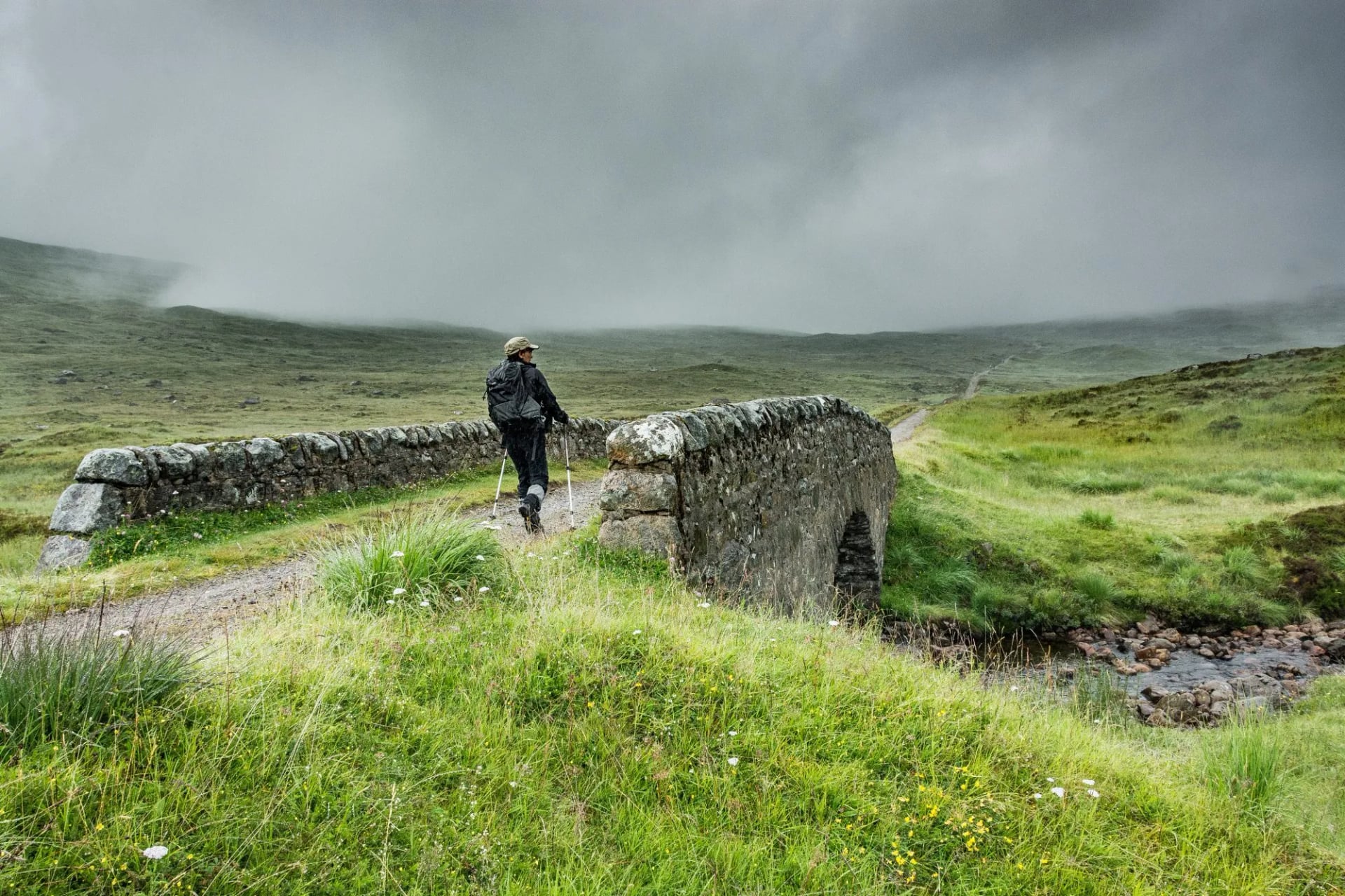 A hiker crossing an old stone bridge on a military road section of the West Highland Way