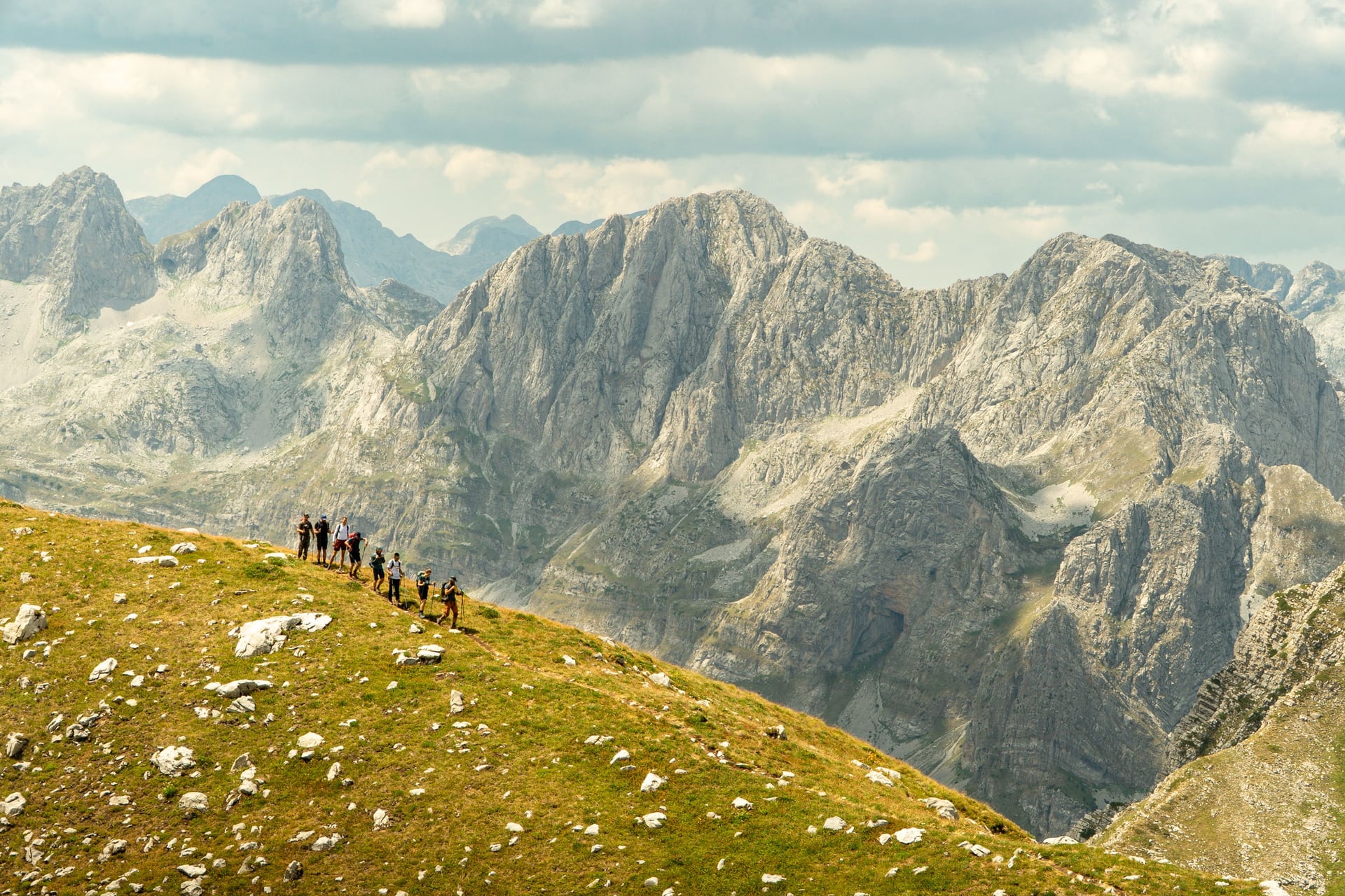 Group of hikers trekking along a mountain ridge with rocky peaks in the background.