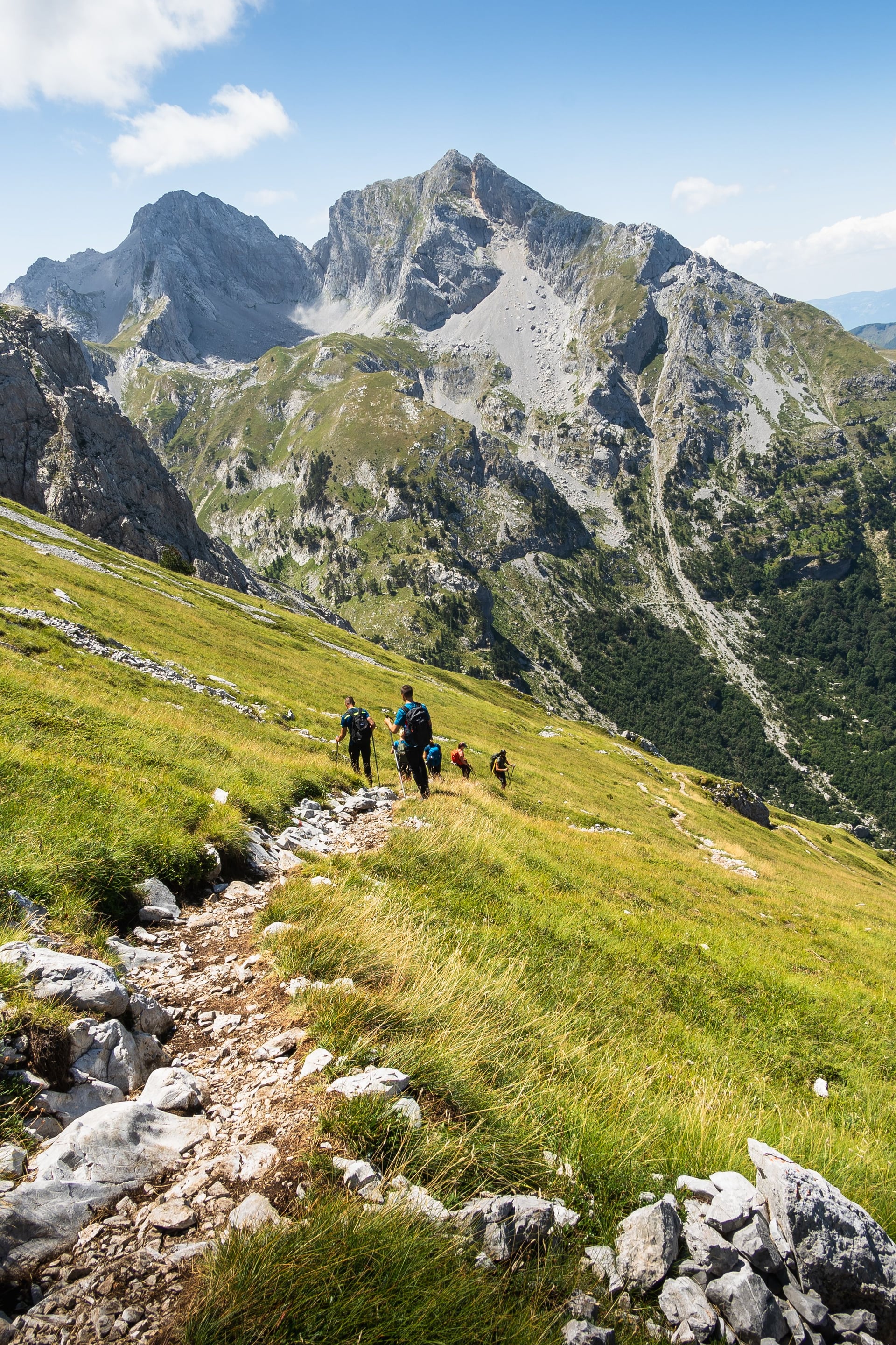 Turisté na horské stezce s kamenitými vrcholy a zelenými svahy