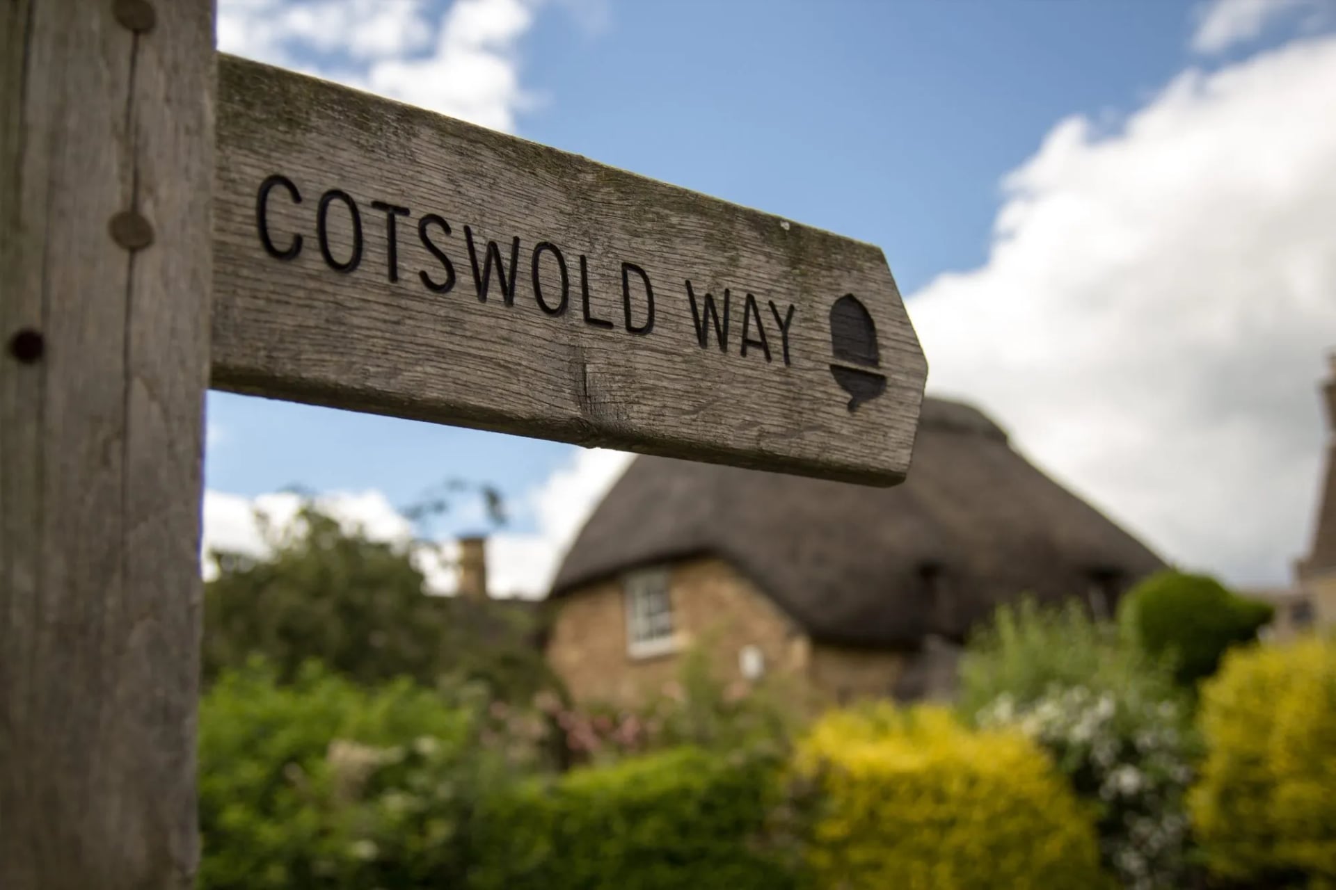 Wooden Cotswold Way fingerpost in front of a thatched cottage