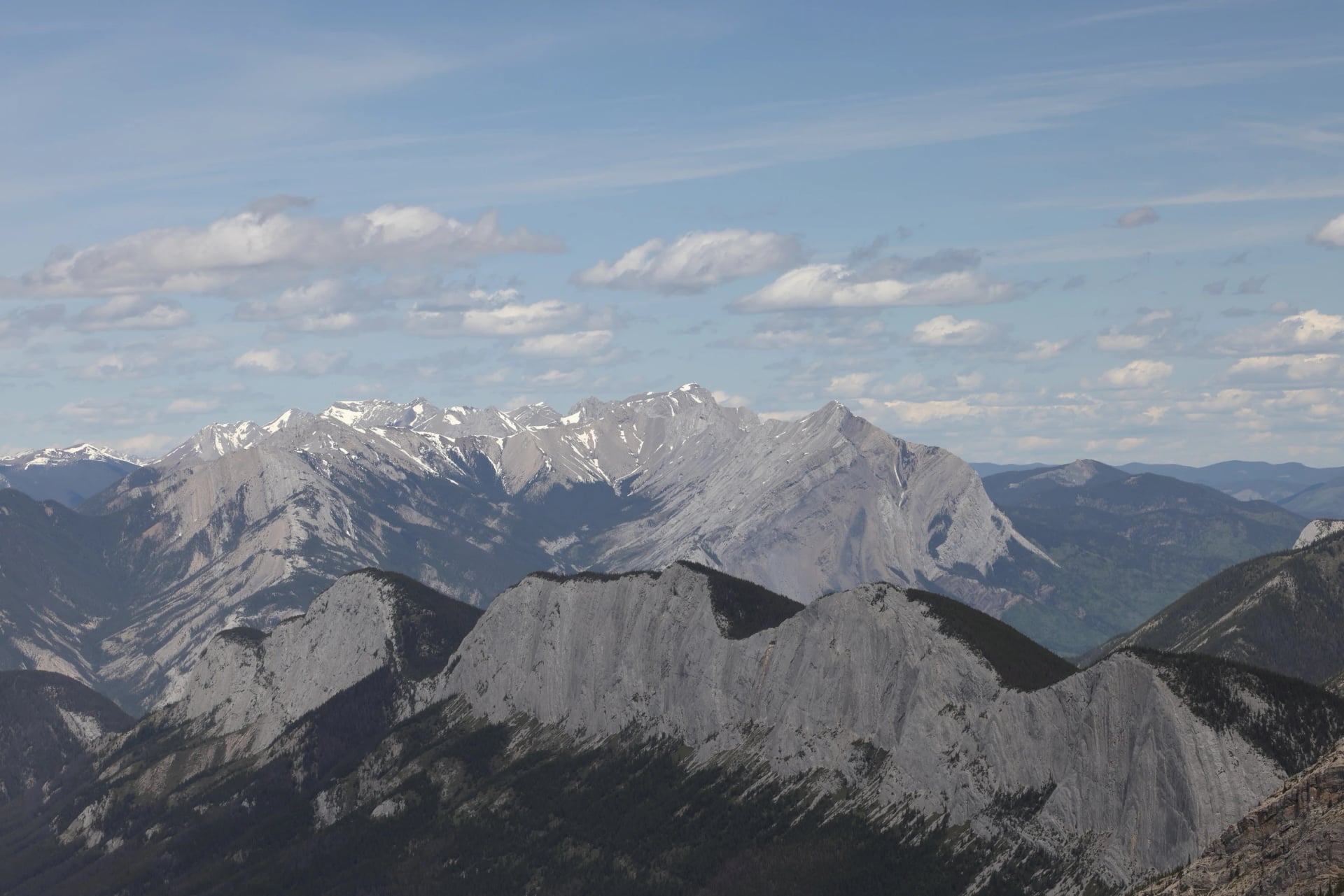 A bare grey limestone mountain face with steeply tilted rock layers under heavy cloud.