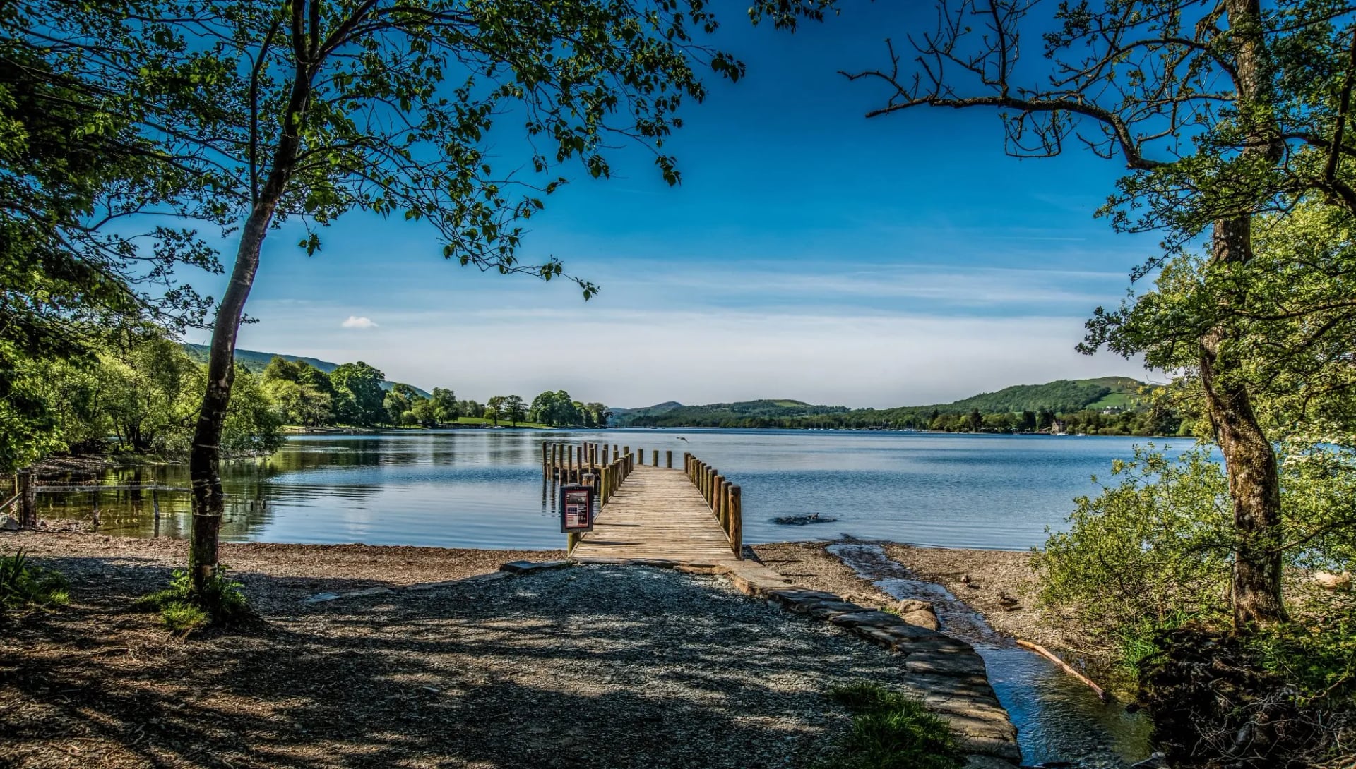 A wooden jetty reaching into Coniston Water between overhanging trees