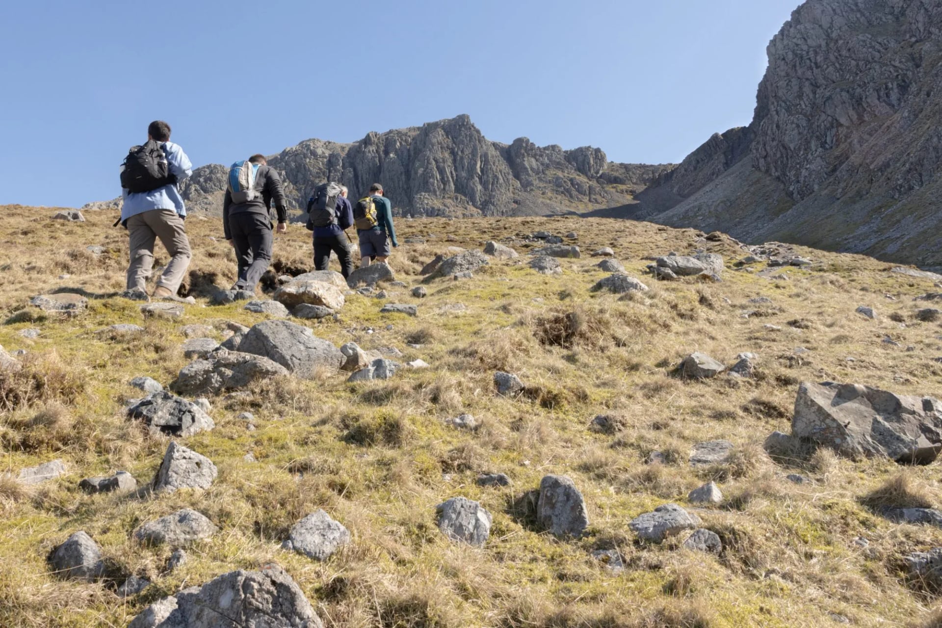 A group of walkers crossing rough boulder ground towards crags