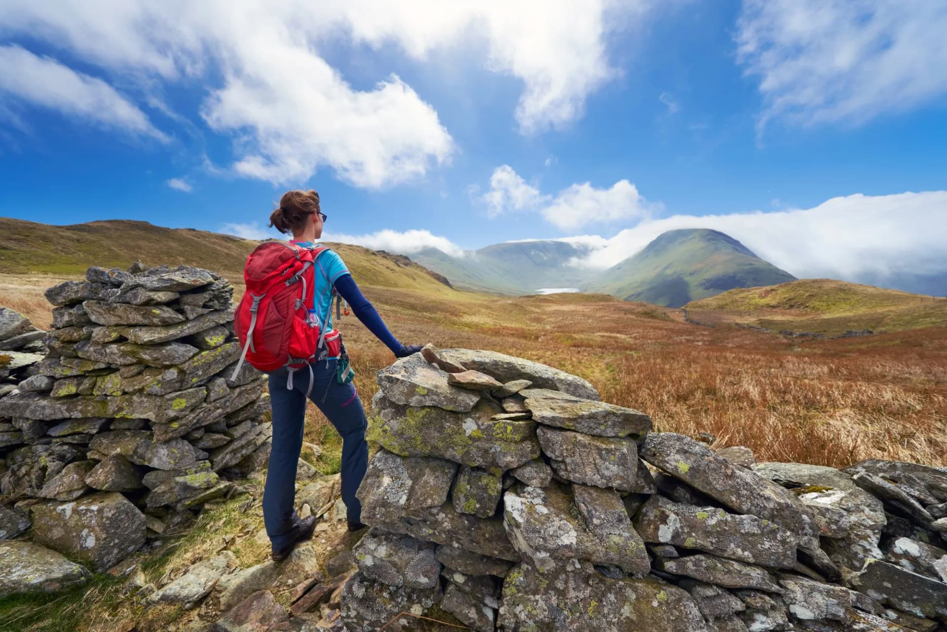 A female hiker taking in the mountain views of Hayeswater, the summits of Gray Crag, Thornthwaite and a cloud covered Stony Cove Pike in the distance. Lake District UK.
