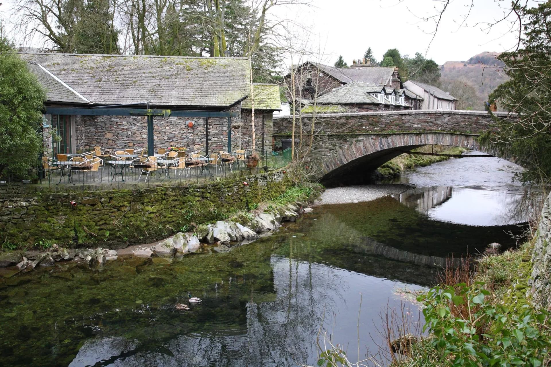 Scenic view of Grasmere village with houses, bridge and ducks floating on the river during early Spring in Ambleside town, Windermere, Lake District National Park, Cumbria, England UK