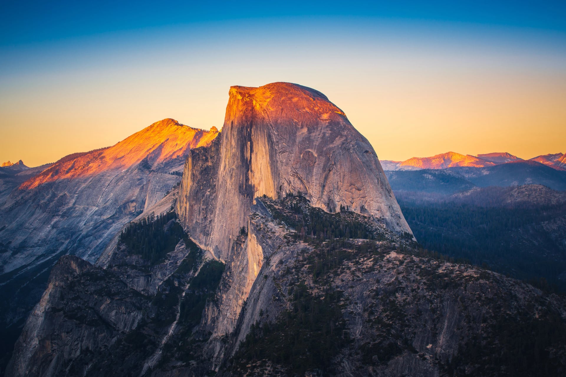 The granite face of Half Dome lit orange at sunset above forested ridges