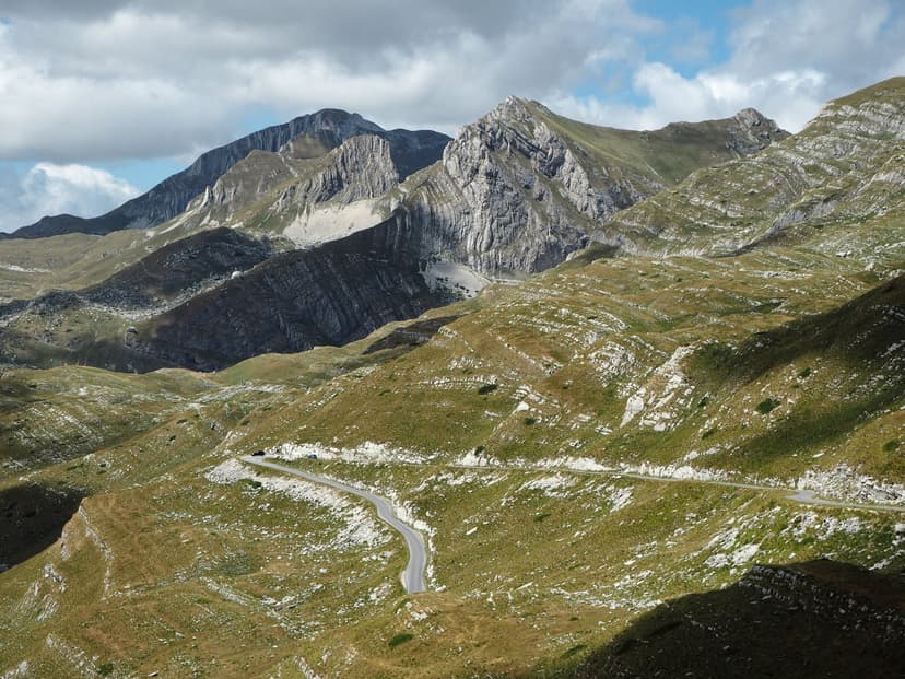 Winding mountain road through Durmitor Sedlo Pass with rugged peaks under cloudy sky