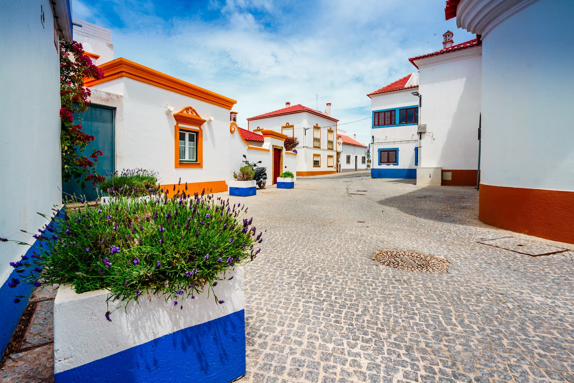 Cobblestone street in Vila Nova de Milfontes old town with white and orange houses under blue sky.