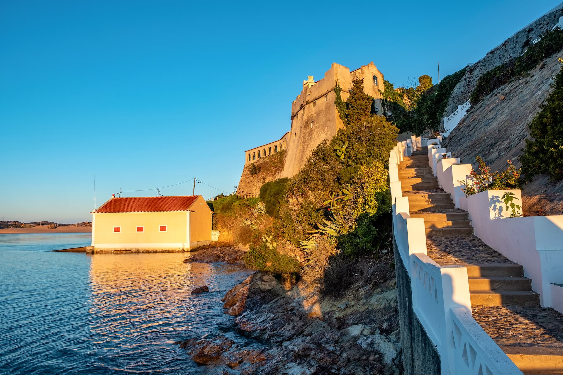 Coastal path steps leading up to a historic fort above the water in Vila Nova de Milfontes.