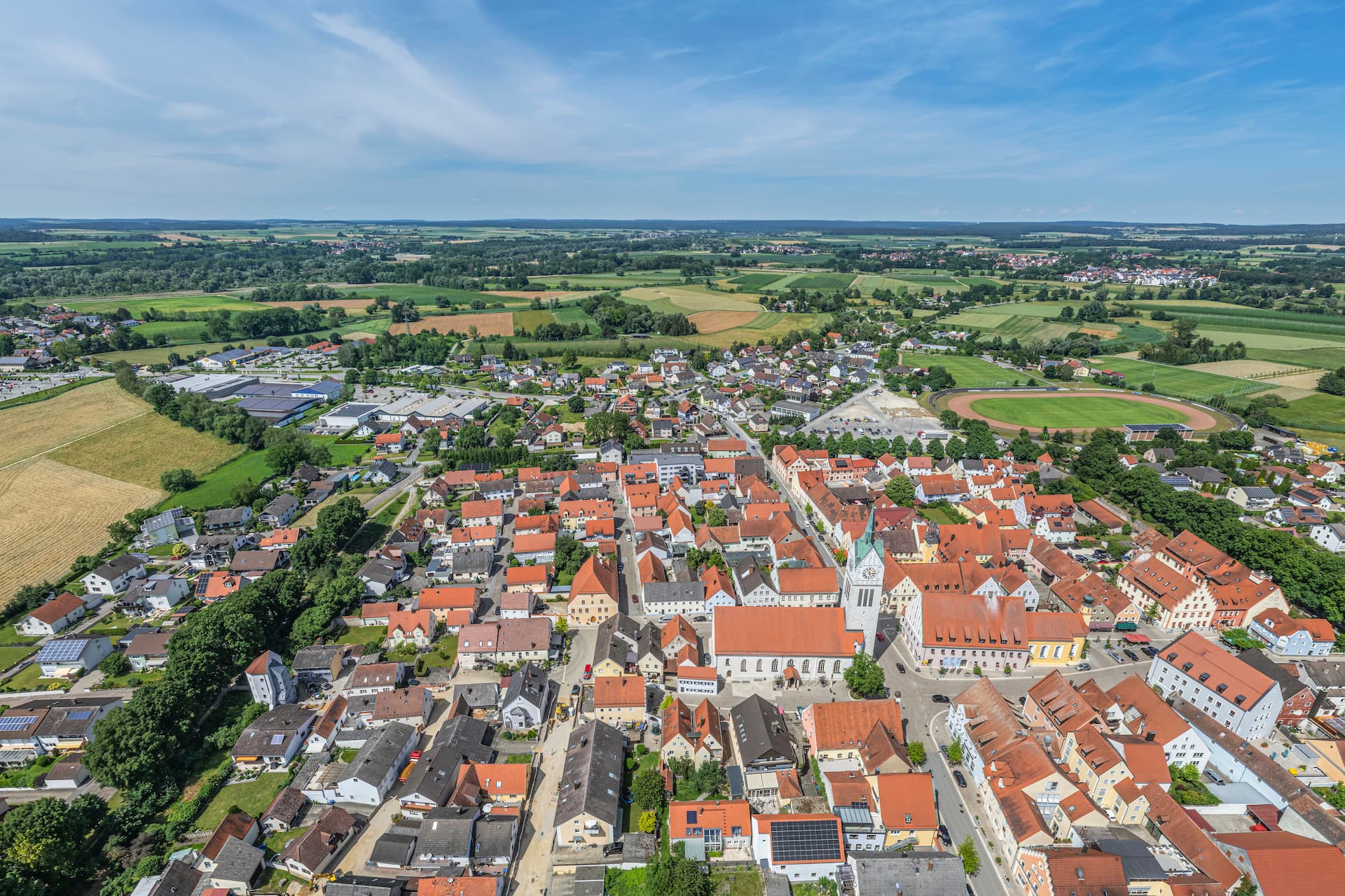 Aerial view of Kelheim town center with red-roofed buildings, church tower, and surrounding green fields.