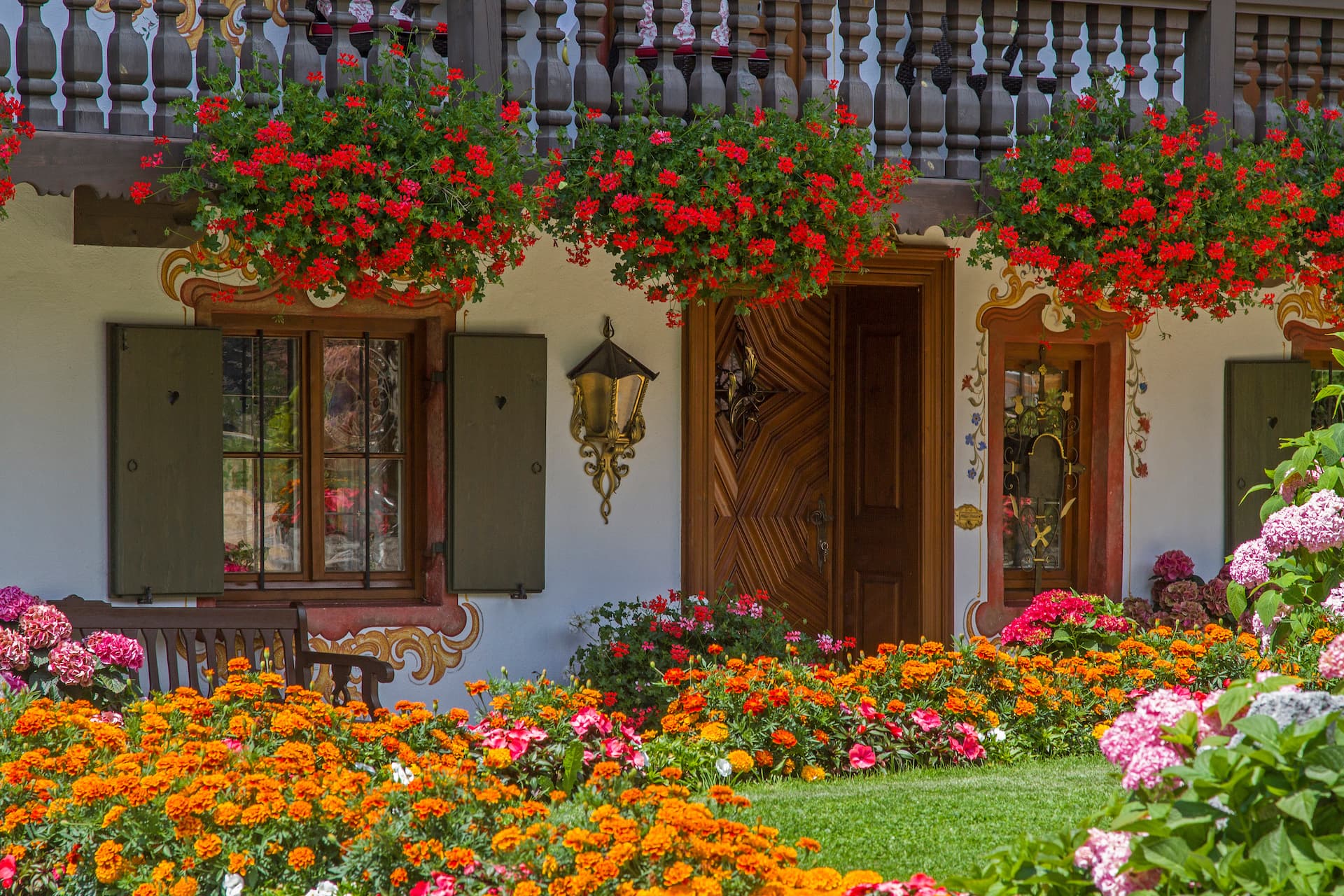 Traditional Bavarian house facade with bright orange flowers, red geraniums, and green shutters in Bayrischzell.