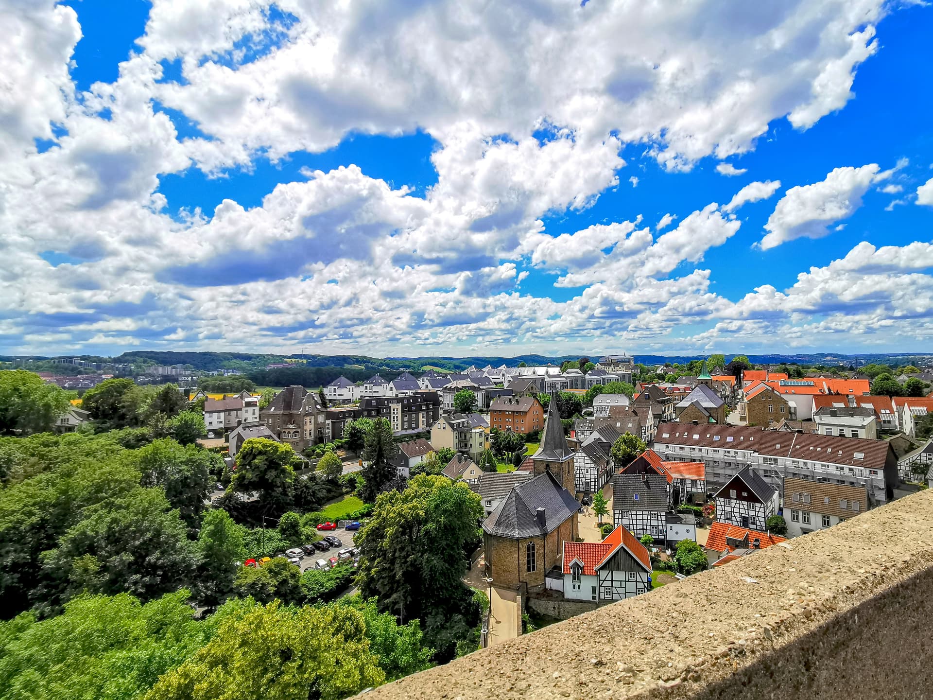 Townscape view over rooftops and green trees under a bright blue sky with white clouds, Blankenburg.