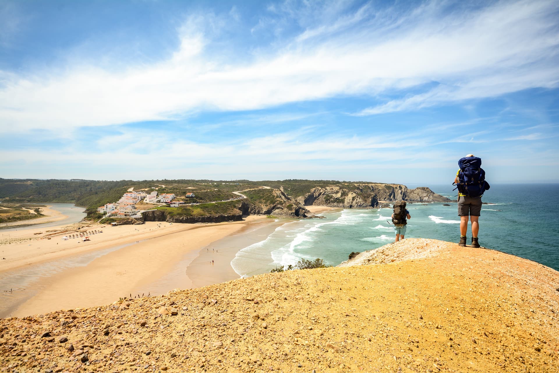 Hiker with large backpack overlooking a beach and coastal village in Portugal.