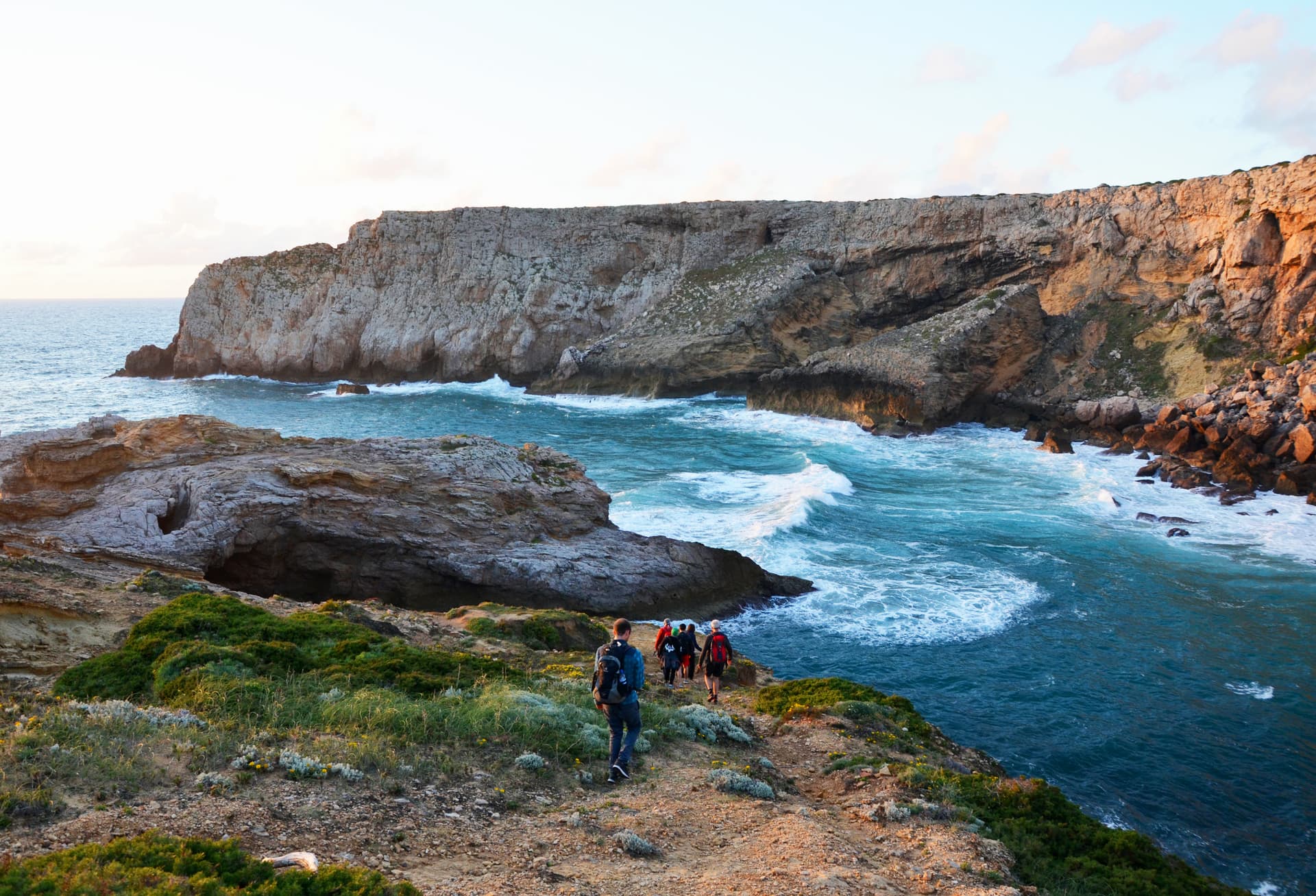 Hikers on coastal trail above turquoise sea near cliffs at Praia do Amado, Algarve.