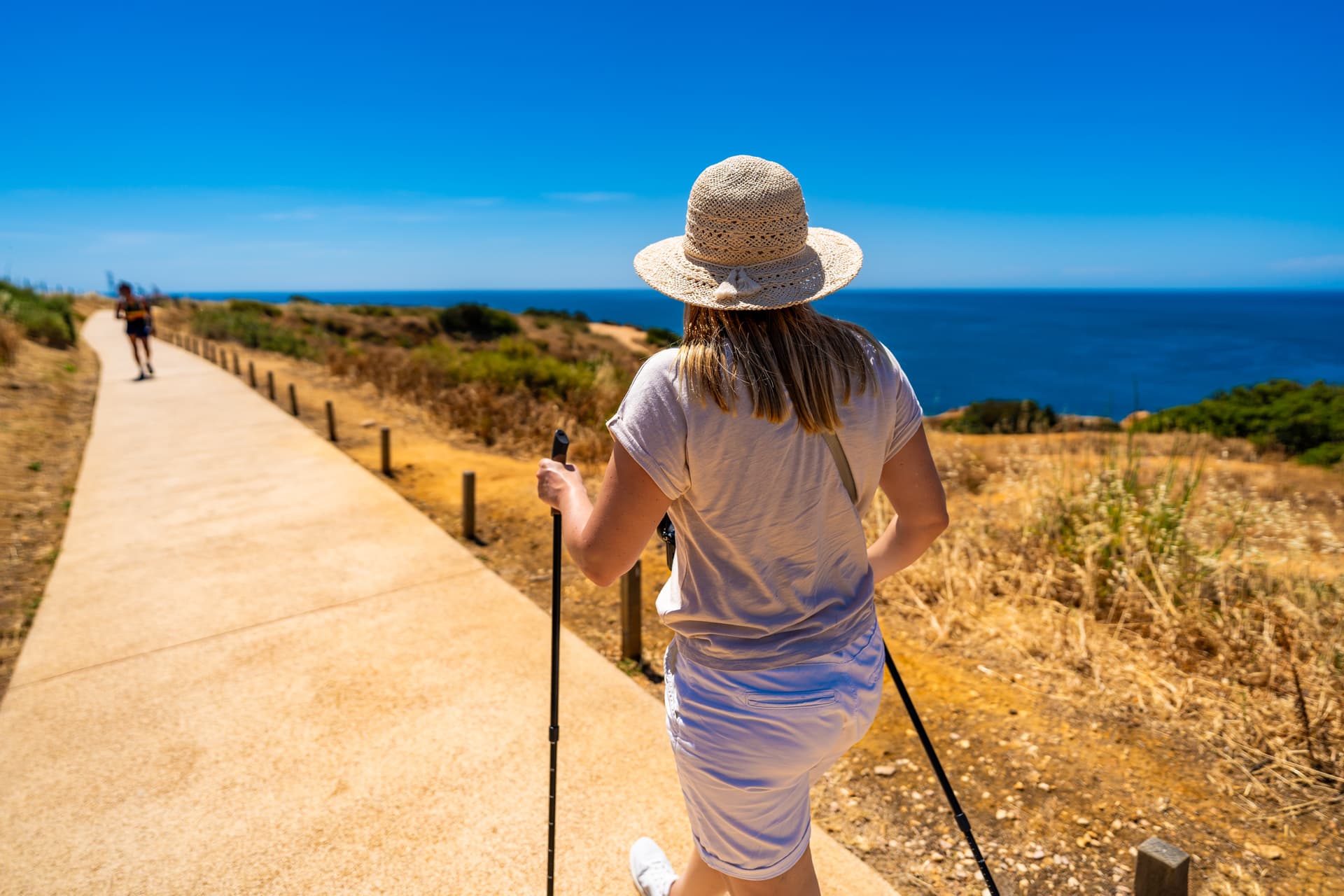Woman hiking with poles on coastal path overlooking deep blue sea in Lagos, Portugal.