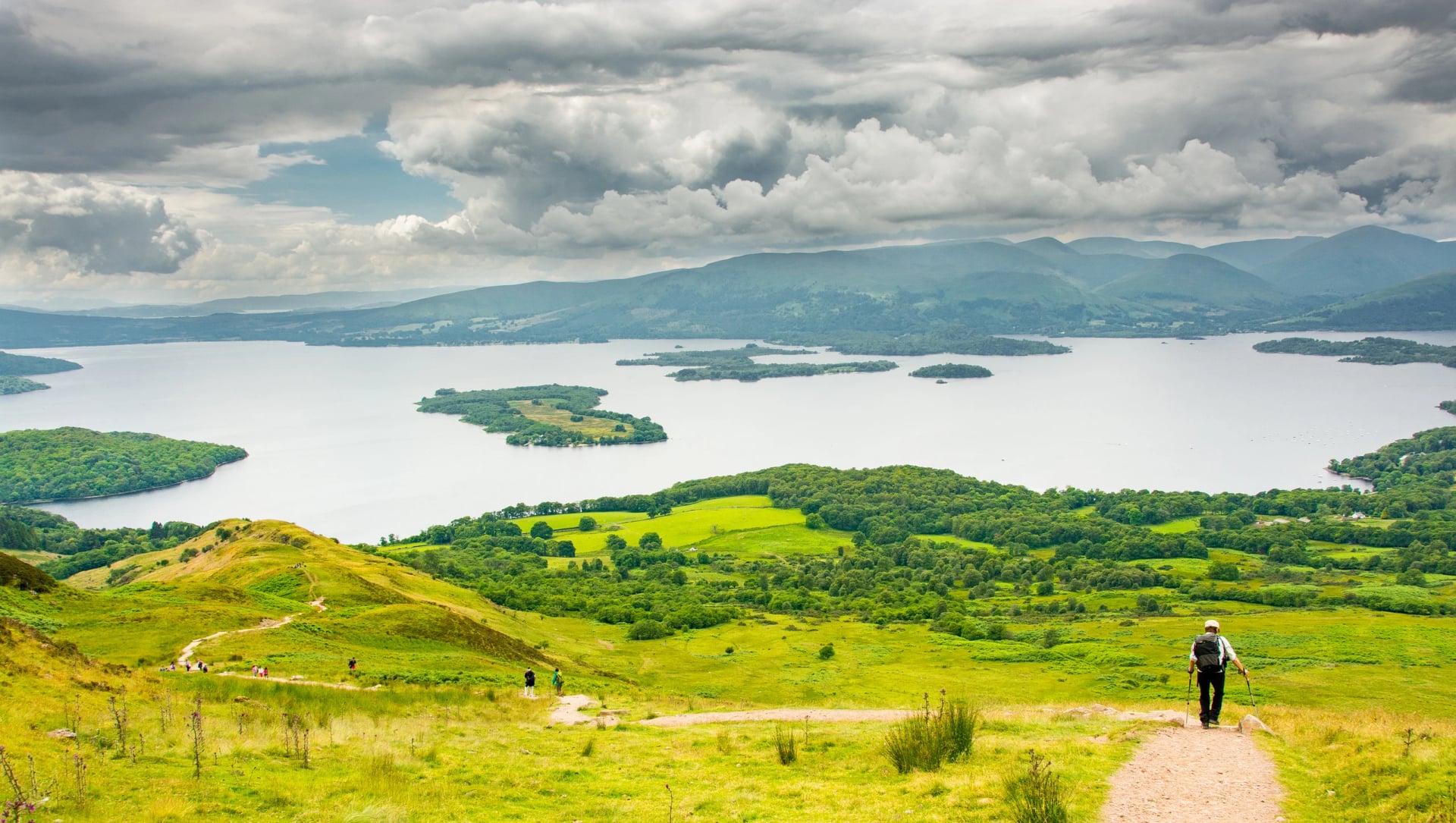 A walker on a path descending towards the islands of Loch Lomond