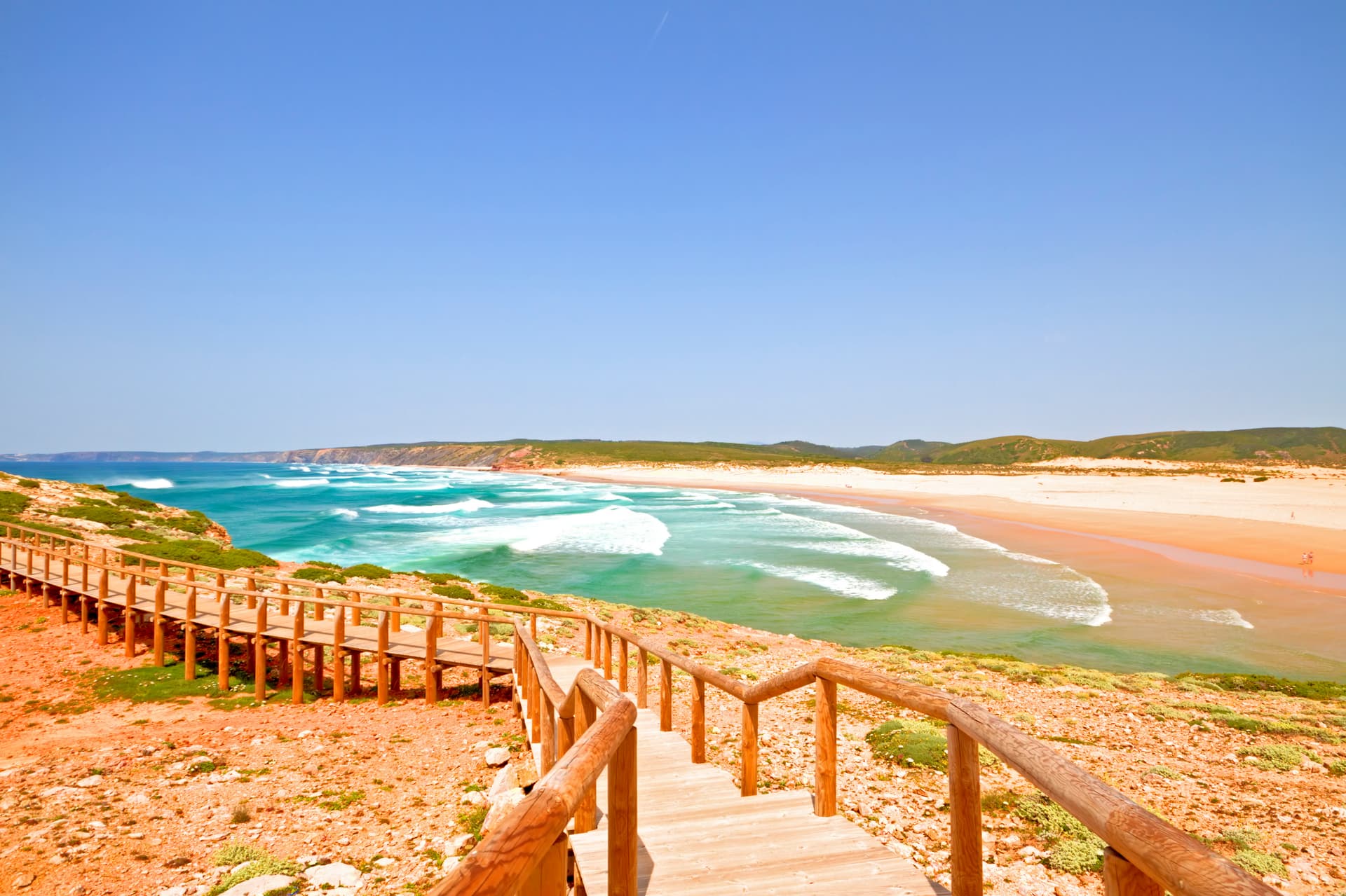 Wooden boardwalk overlooking Carrapateira beach with turquoise waves and coastal cliffs in the Algarve, Portugal.