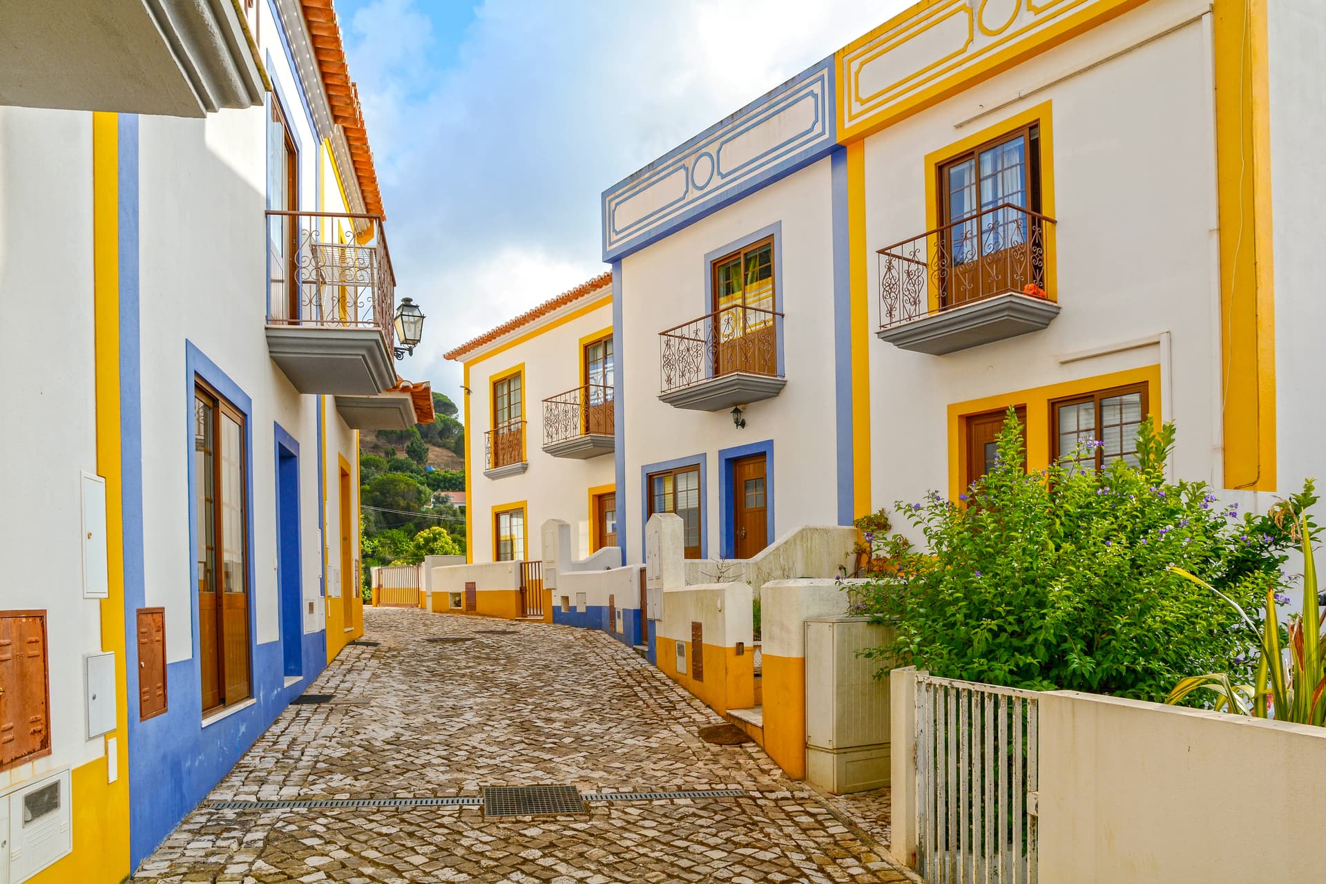 Residential buildings with yellow and blue trim on a cobblestone street in Bordeira near Carrapateira.