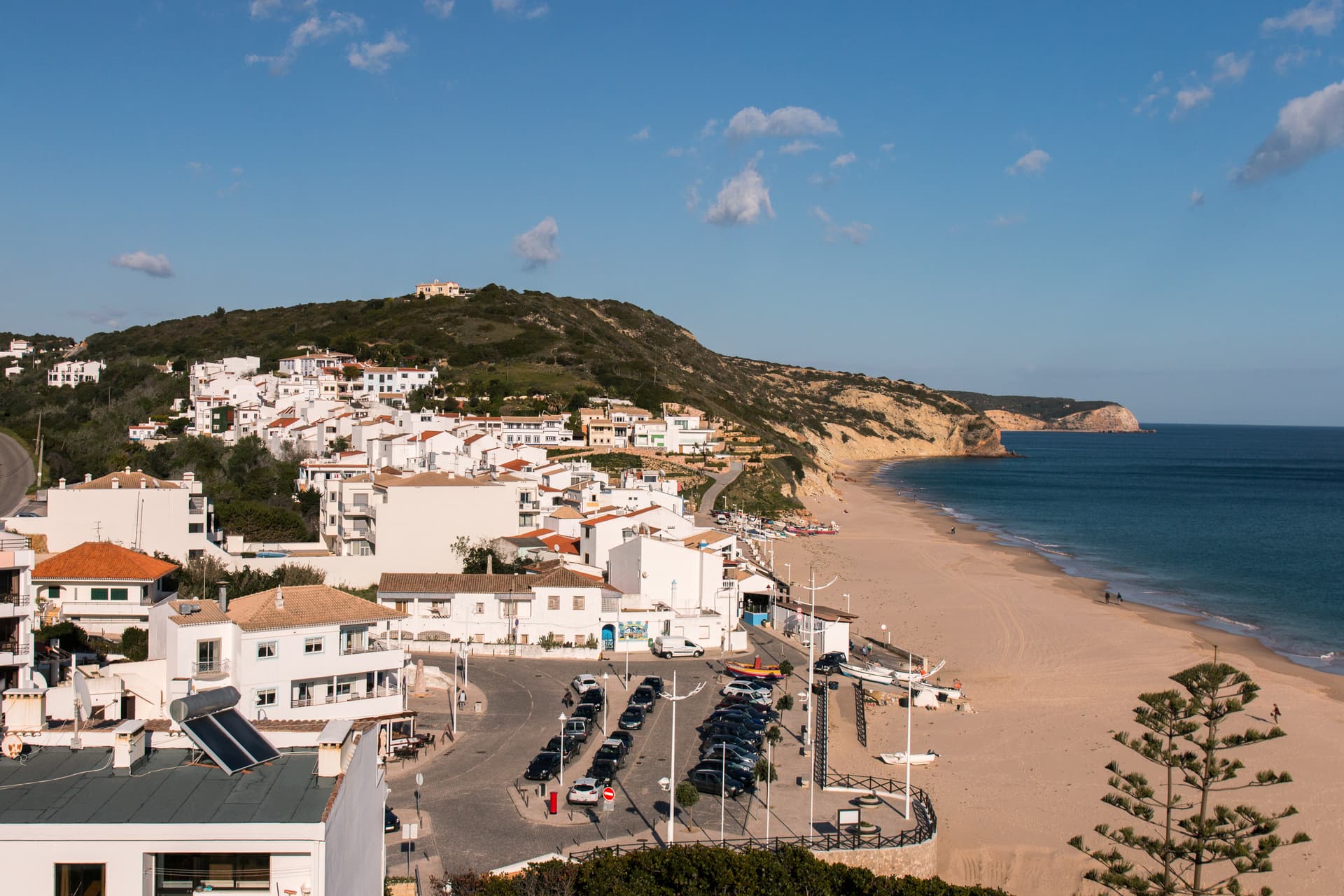 White village houses on hillside overlooking sandy beach and blue sea in Salema, Portugal.