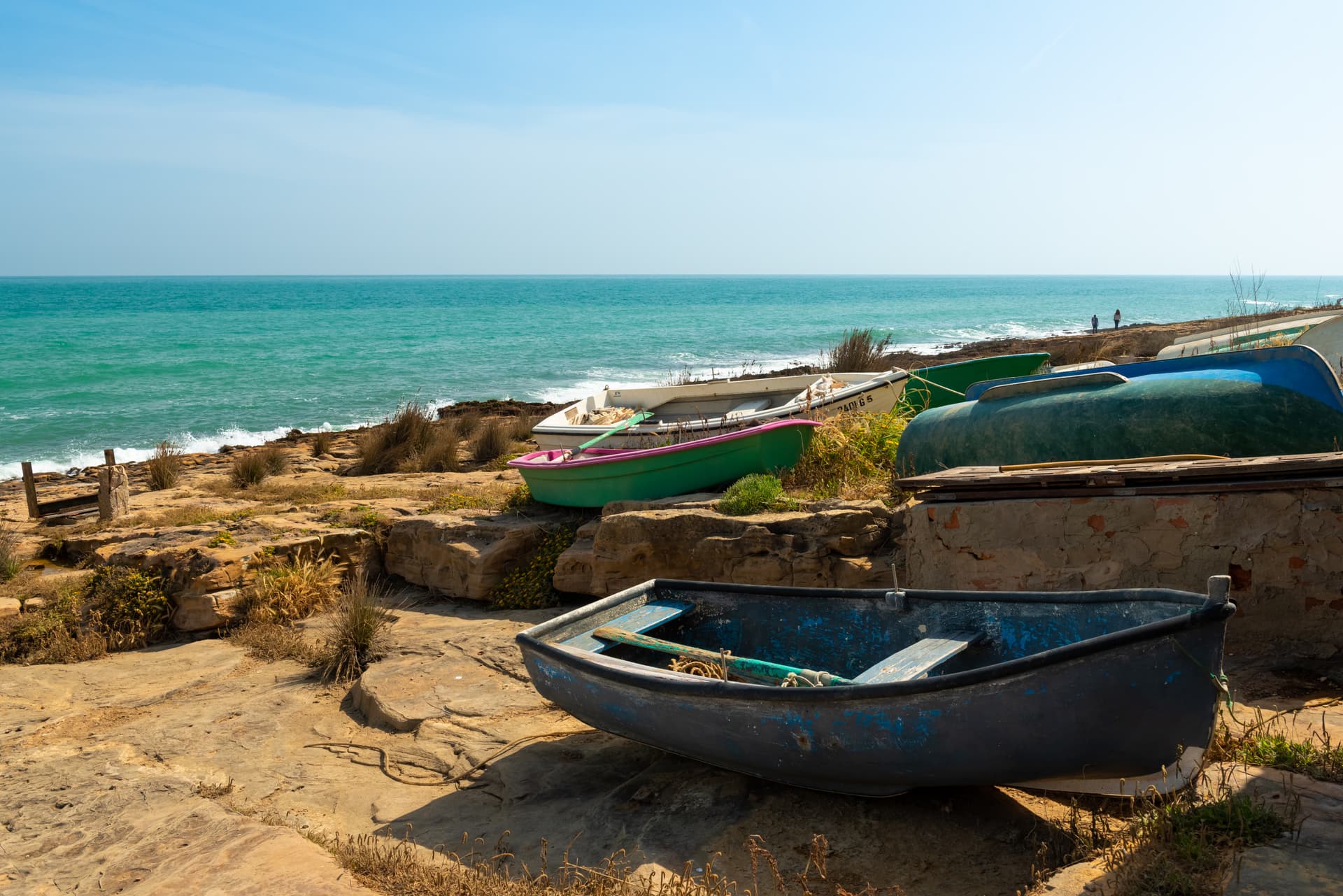 Fishing boats resting on dry, rocky shore above turquoise sea in Algarve, Portugal.