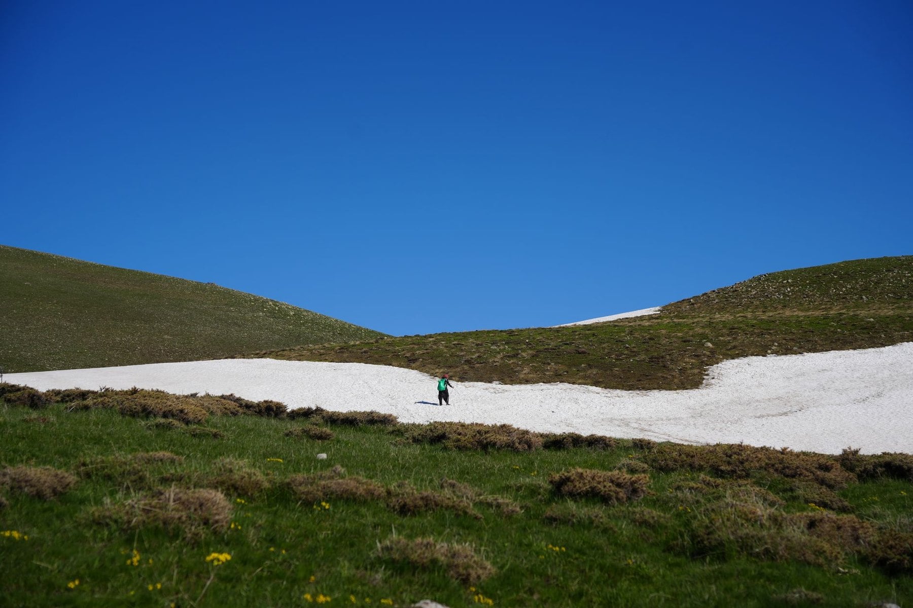 A walker crossing an old snow patch on a high slope