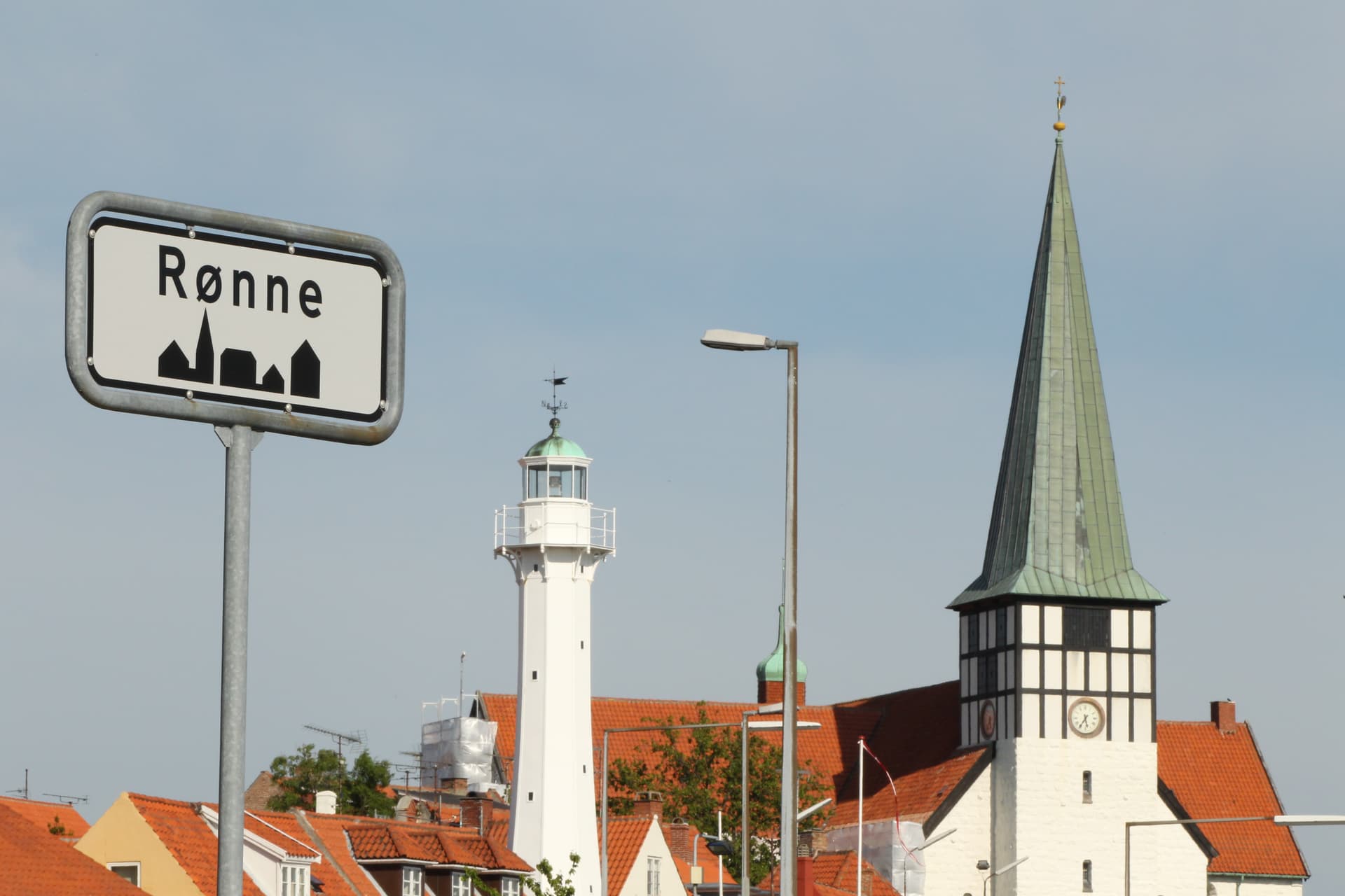 Rønne town sign with white lighthouse and church steeple against blue sky.