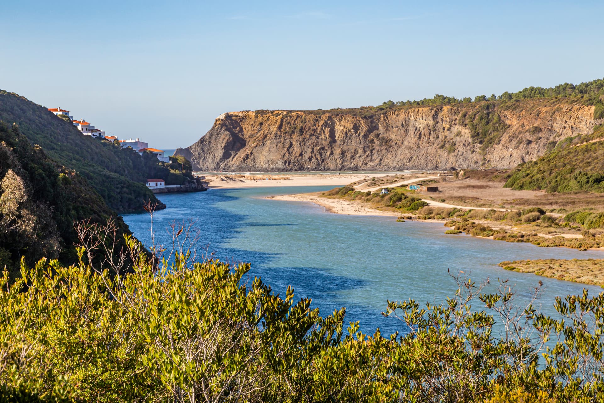 River meeting the sea at Odeceixe, Algarve, Portugal, with cliffs and vegetation.