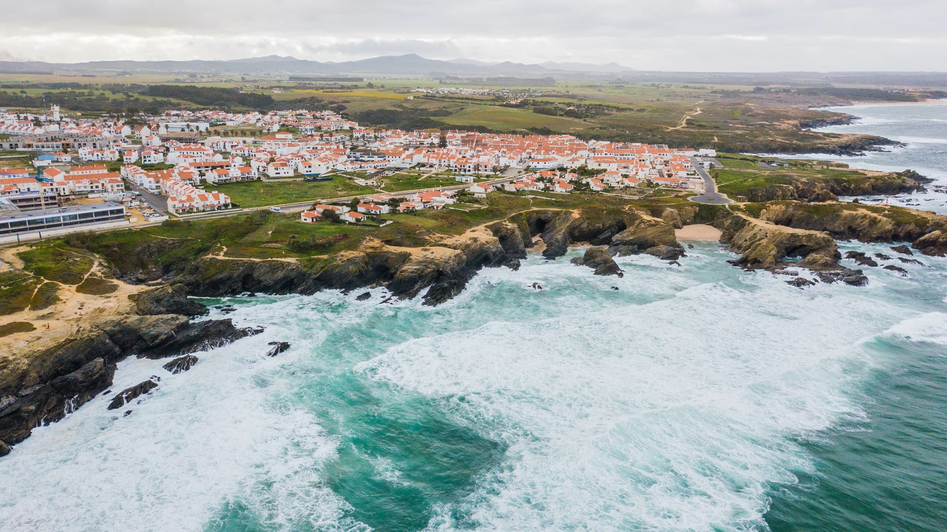 Cliffs in front of Porto Covo village, Portugal, with white surf crashing on the rocky coastline.