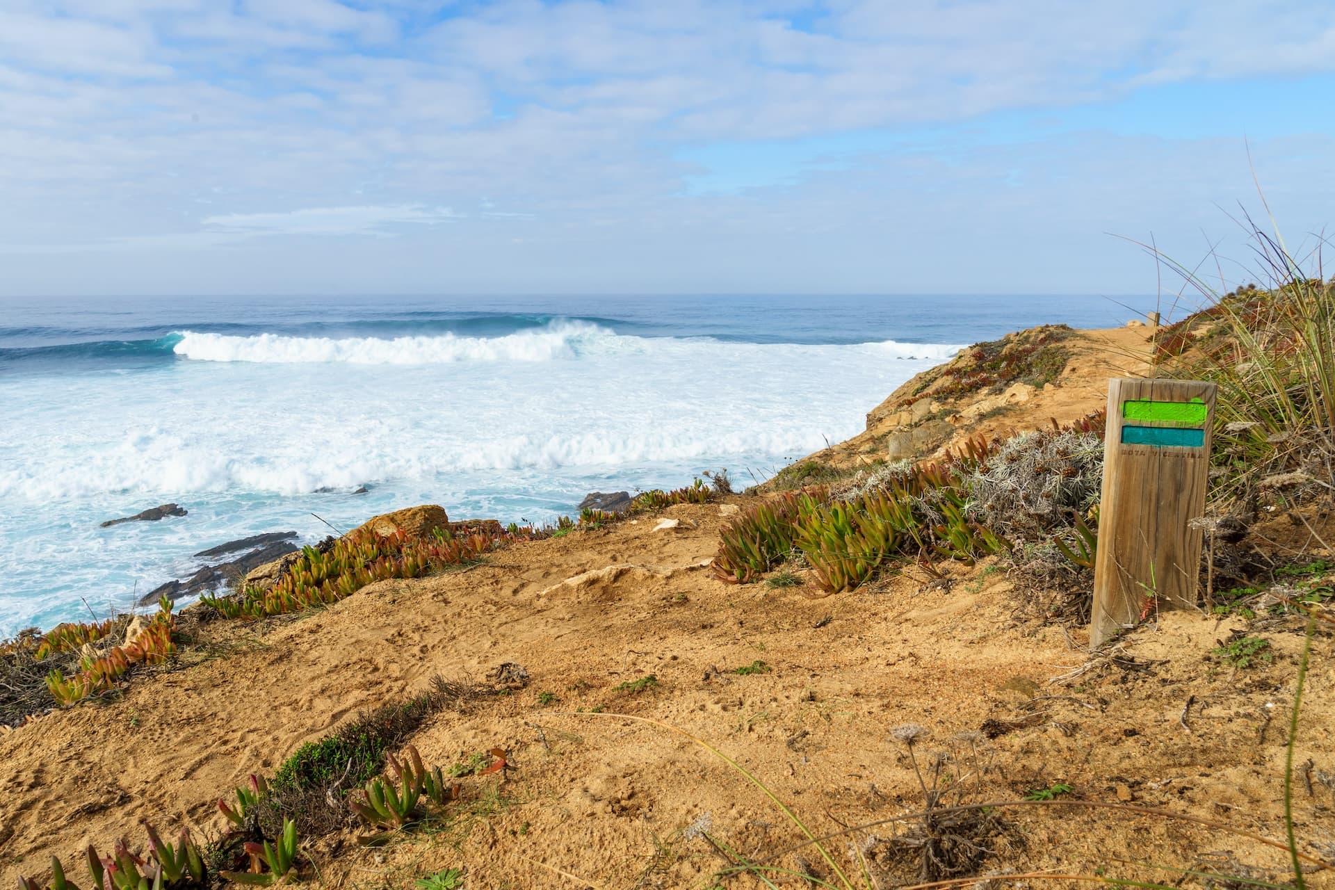 Hiking trail marker on cliff overlooking Rota Vicentina Atlantic coast waves in Portugal
