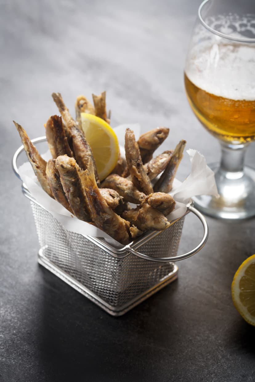 Fried small fish in a wire basket with lemon and a glass of beer