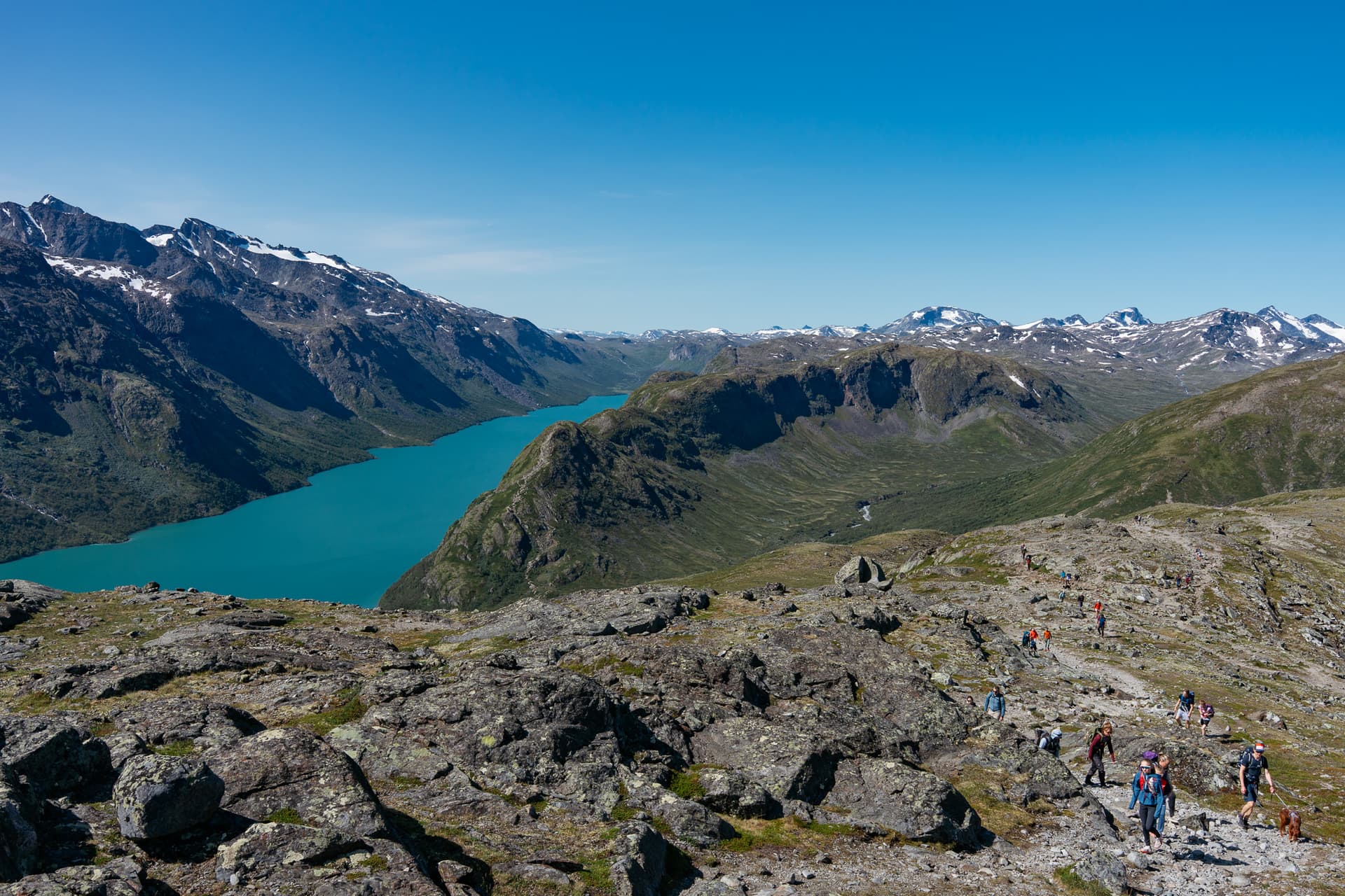 Hikers on Besseggen ridge overlooking turquoise alpine lake and mountains