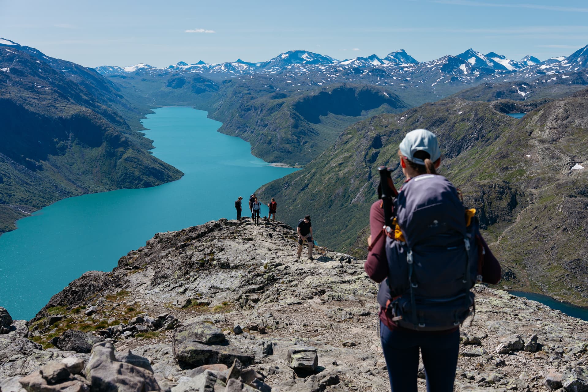 Hikers on the Besseggen ridge overlooking a turquoise glacial lake and mountain peaks in Norway