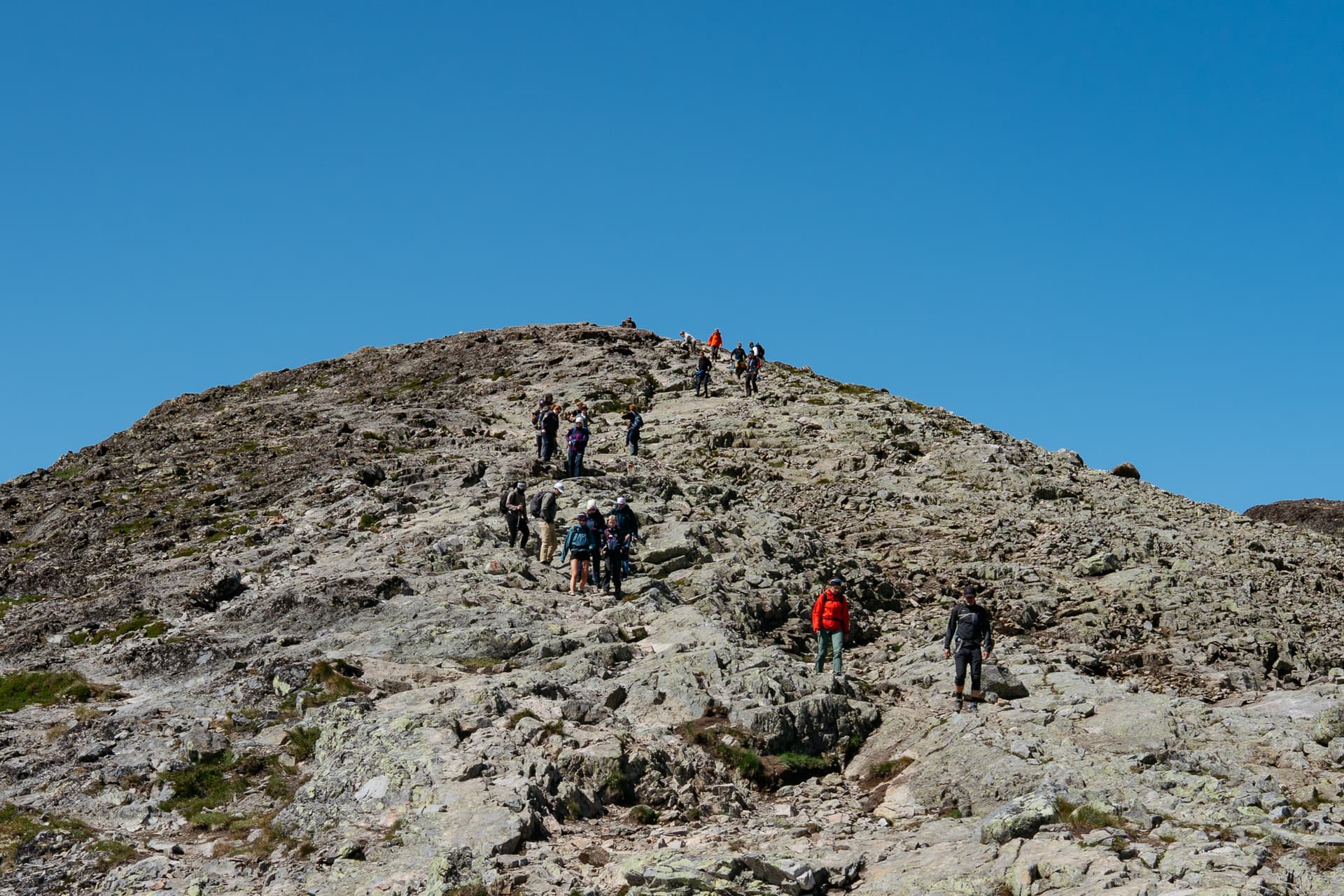 Hikers ascending a rocky mountain dome under a clear blue sky on the Besseggen ridge