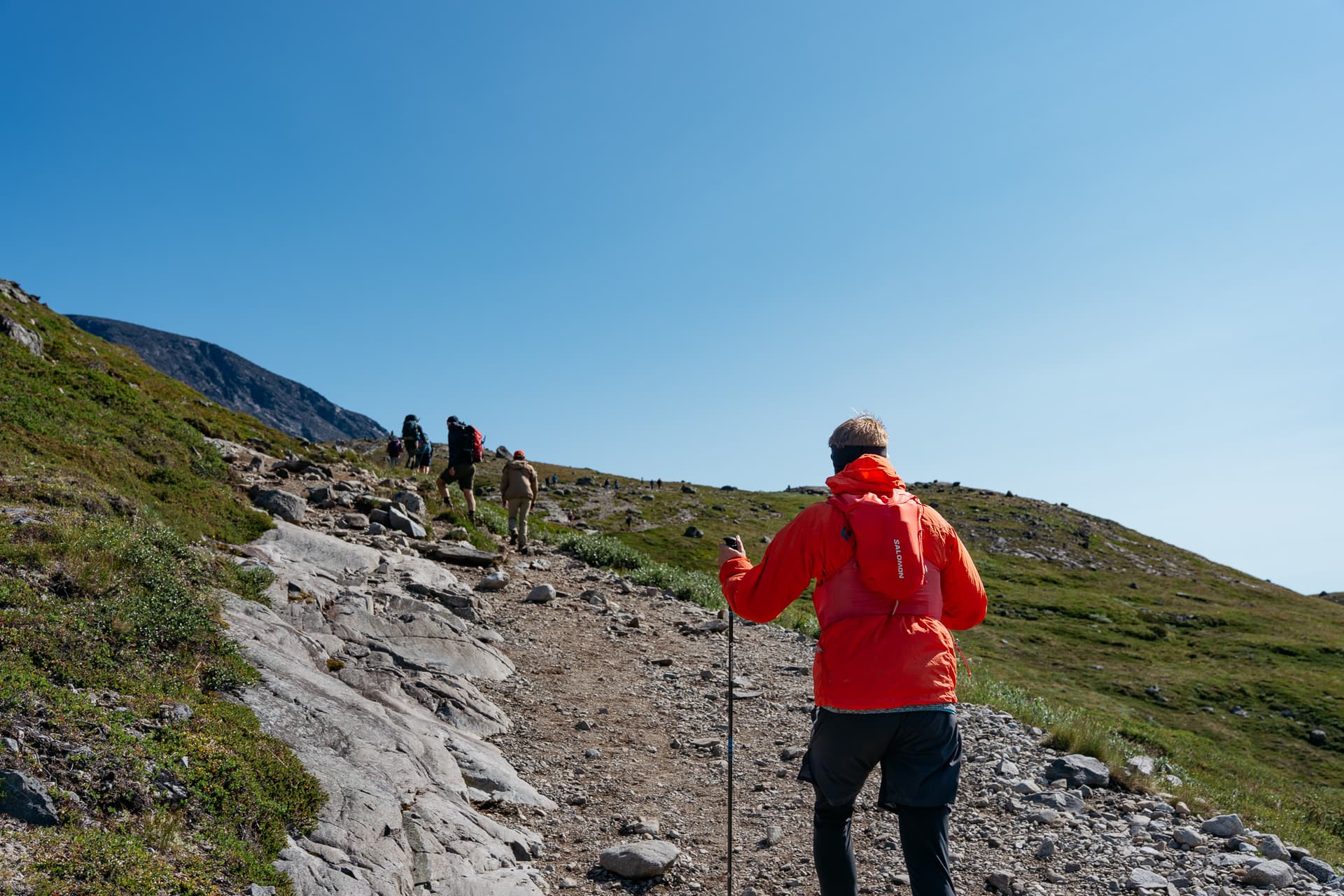 Hikers climbing a rocky mountain trail under a clear blue sky