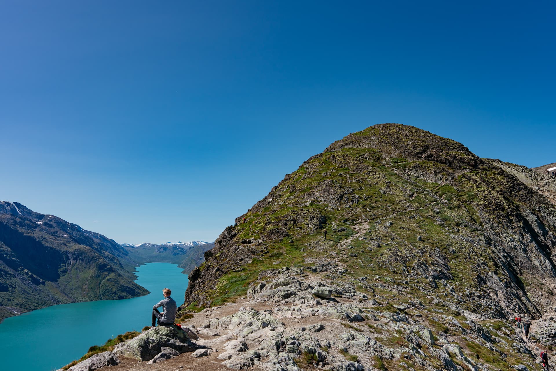 Hiker sitting on rocky ridge above turquoise lake at Besseggen in Norway