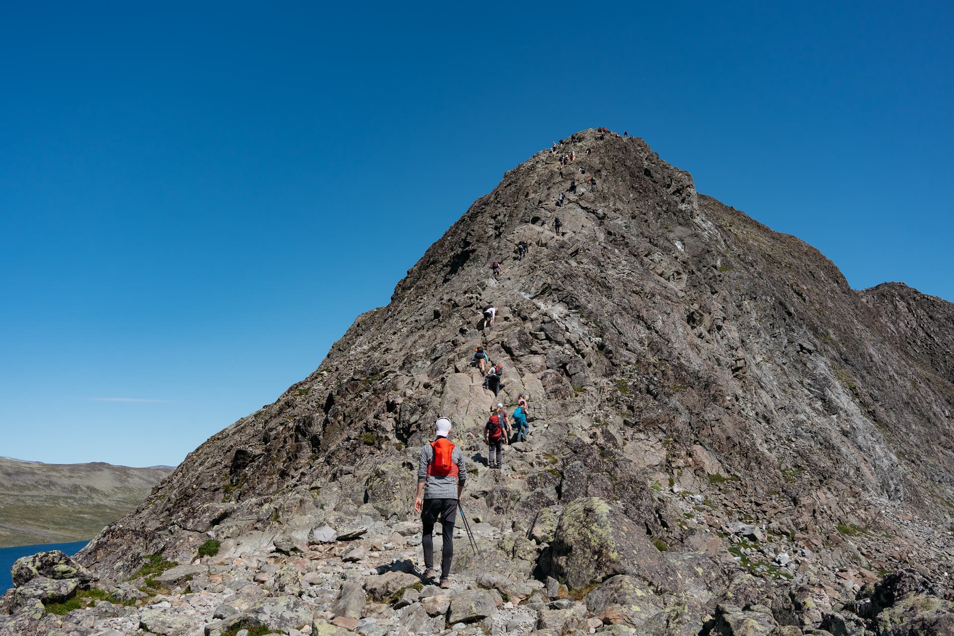 Hikers scrambling up steep rocky ridge of Besseggen under clear blue sky