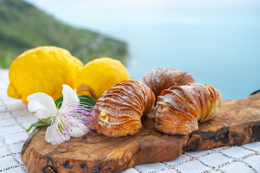 Sfogliatelle pastries with fresh lemons and a caper flower on wooden board with coastal view