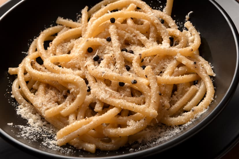 Cacio e pepe pasta in black bowl with grated cheese and black peppercorns