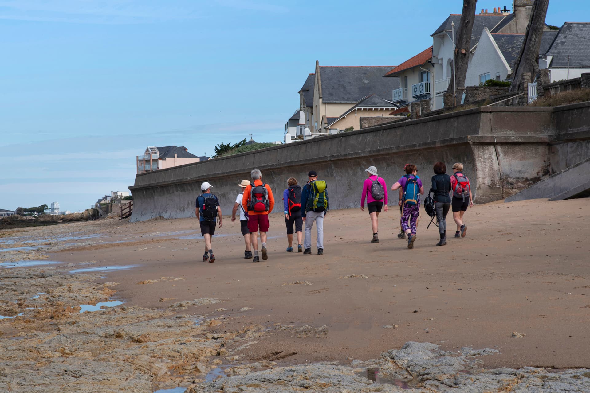 Group hiking with backpacks on a sandy beach in Brittany, France.