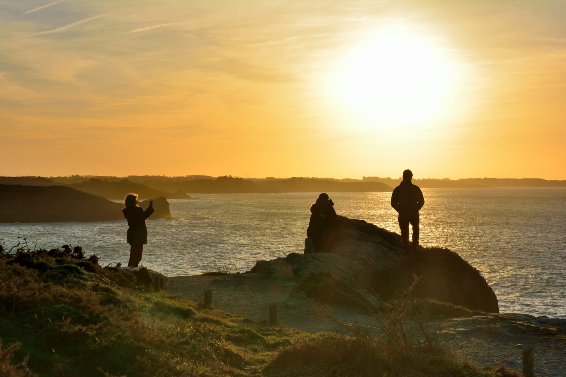 People silhouetted watching sunset over the sea from a cliff in Cancale, Brittany, France.
