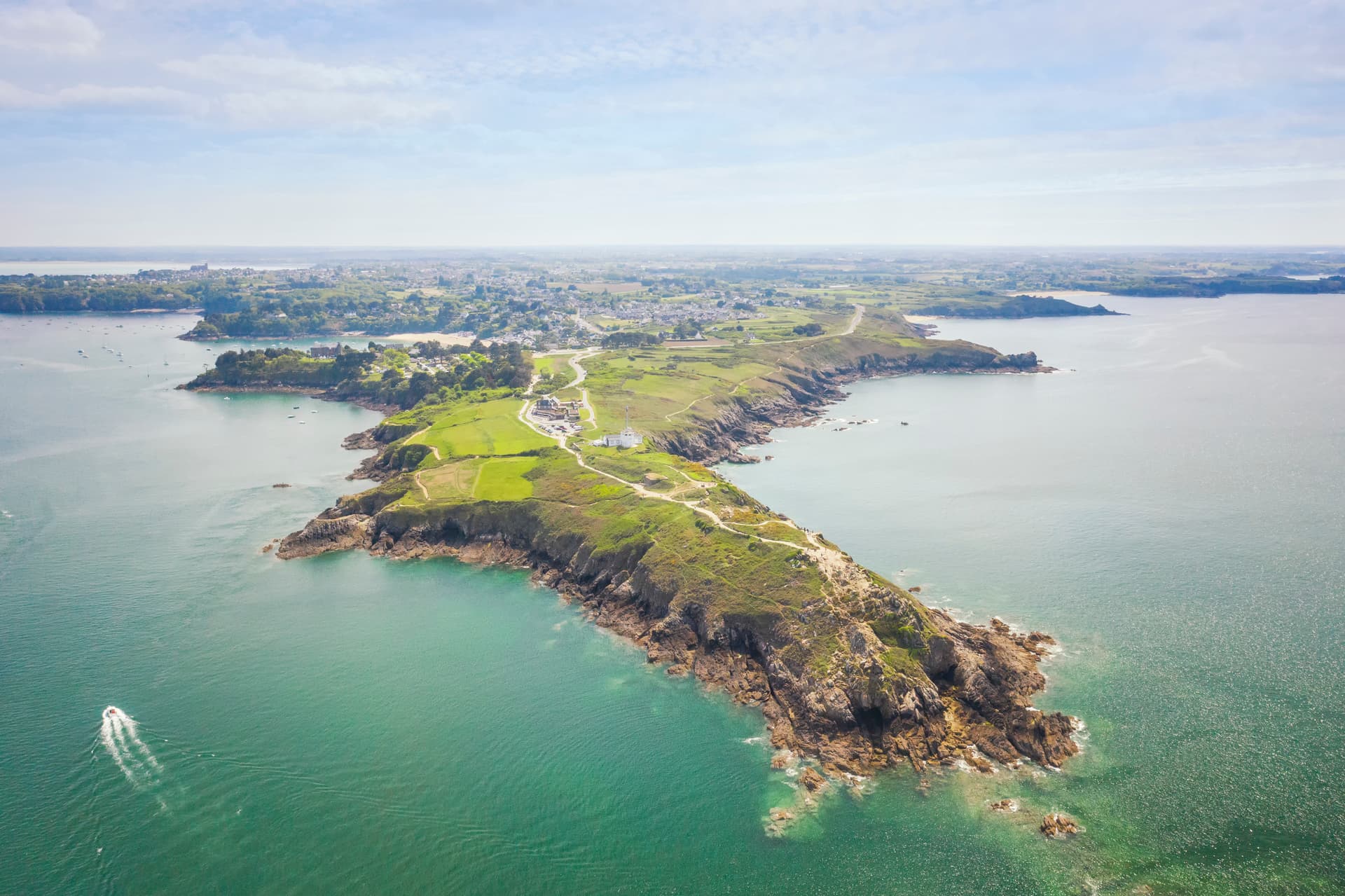 Aerial view of Pointe du Grouin peninsula, rocky coast, green fields, and turquoise sea in Brittany.