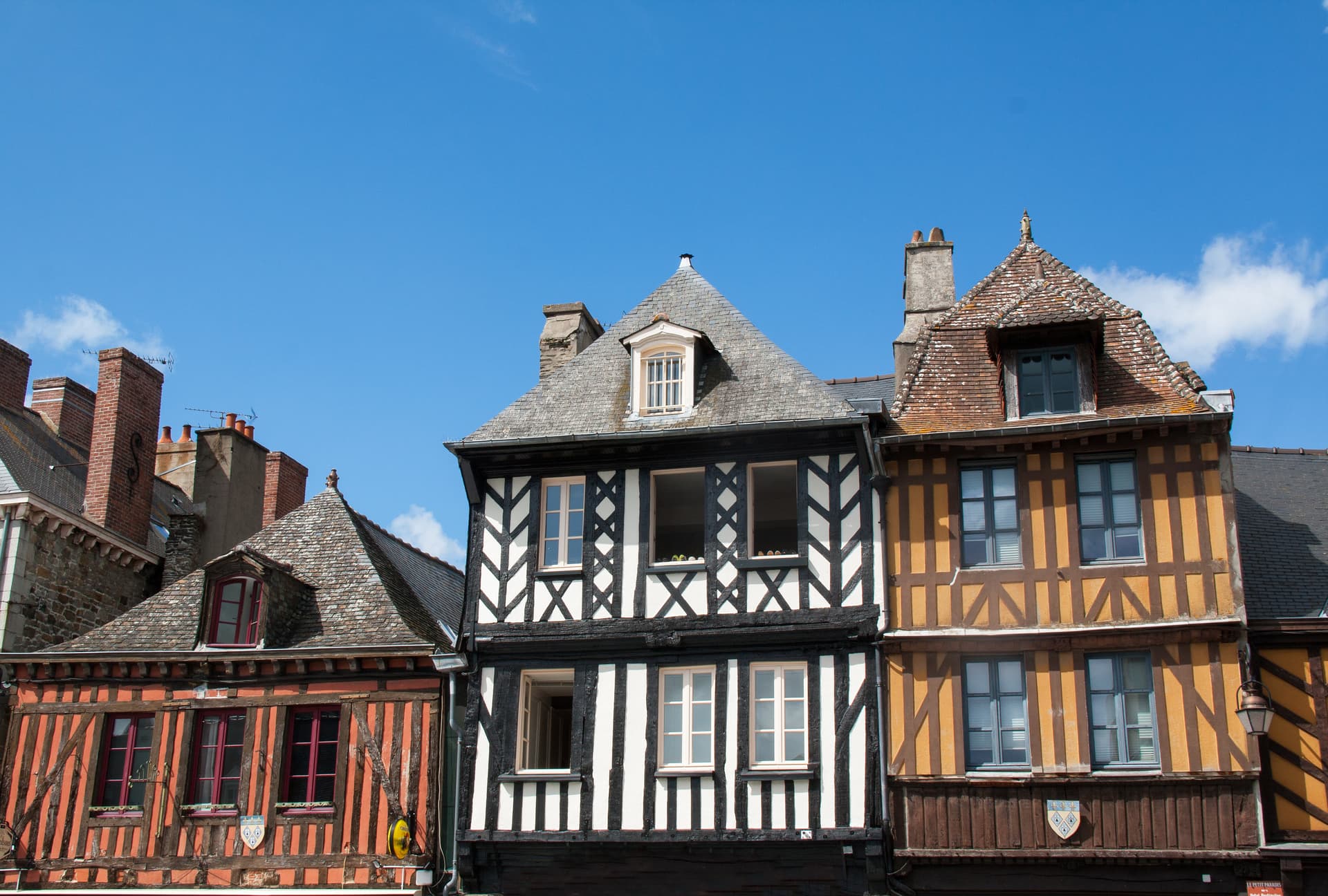 Half-timbered historic houses with colorful facades under a bright blue sky in Dol-de-Bretagne.