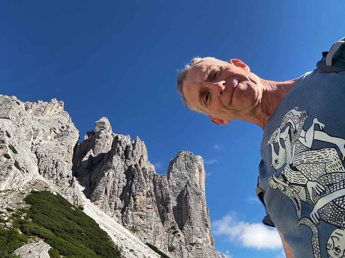 Hiker taking selfie in front of rocky mountain peaks against blue sky