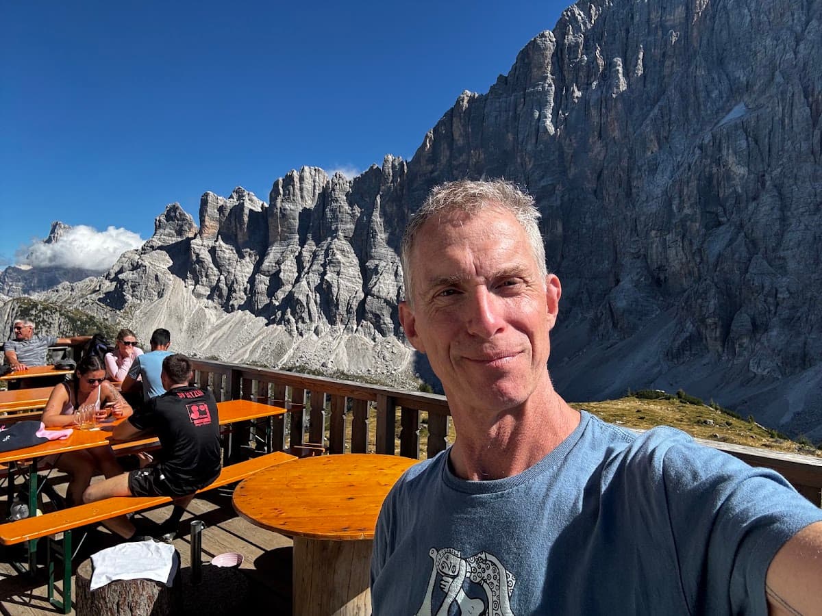 Man taking selfie at outdoor mountain restaurant with rocky peaks in background