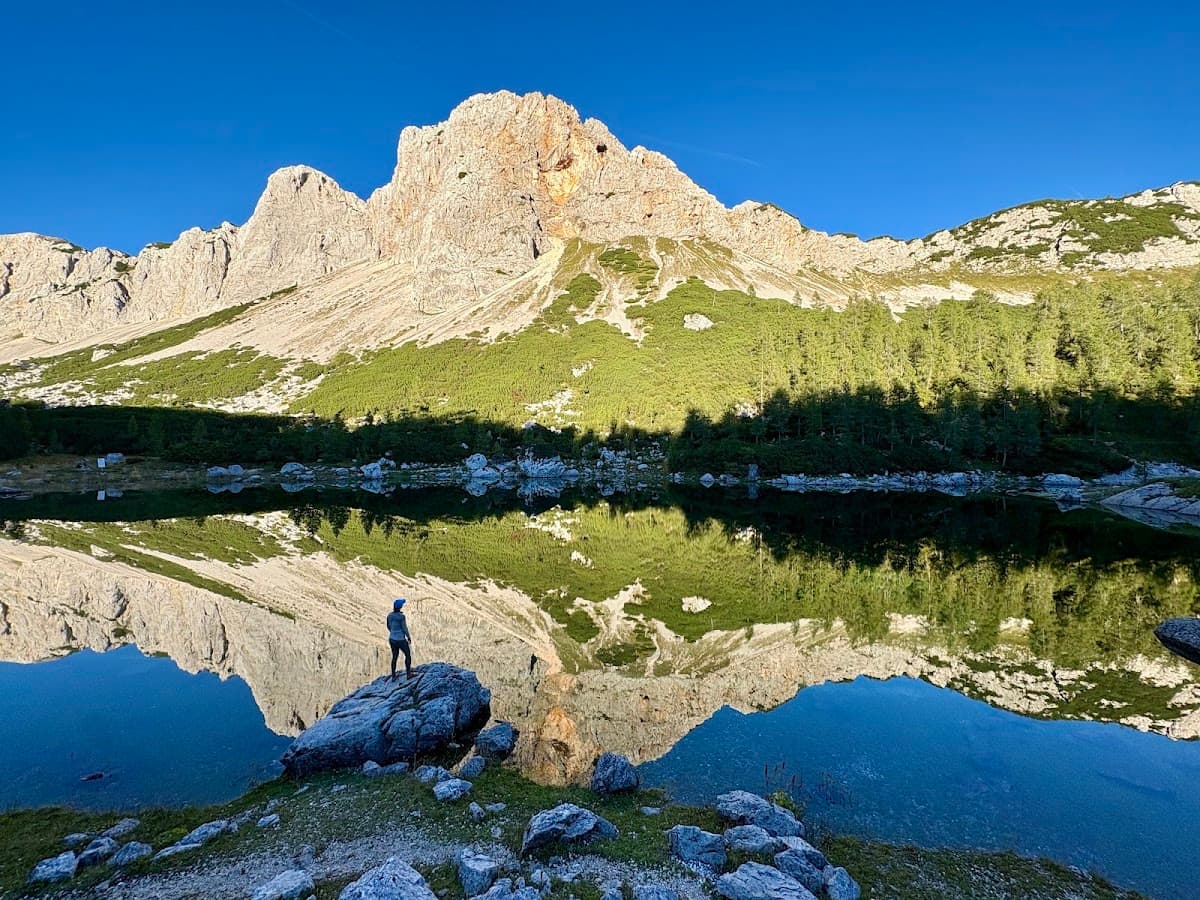 Hiker standing on a rock by an alpine lake reflecting mountain peaks