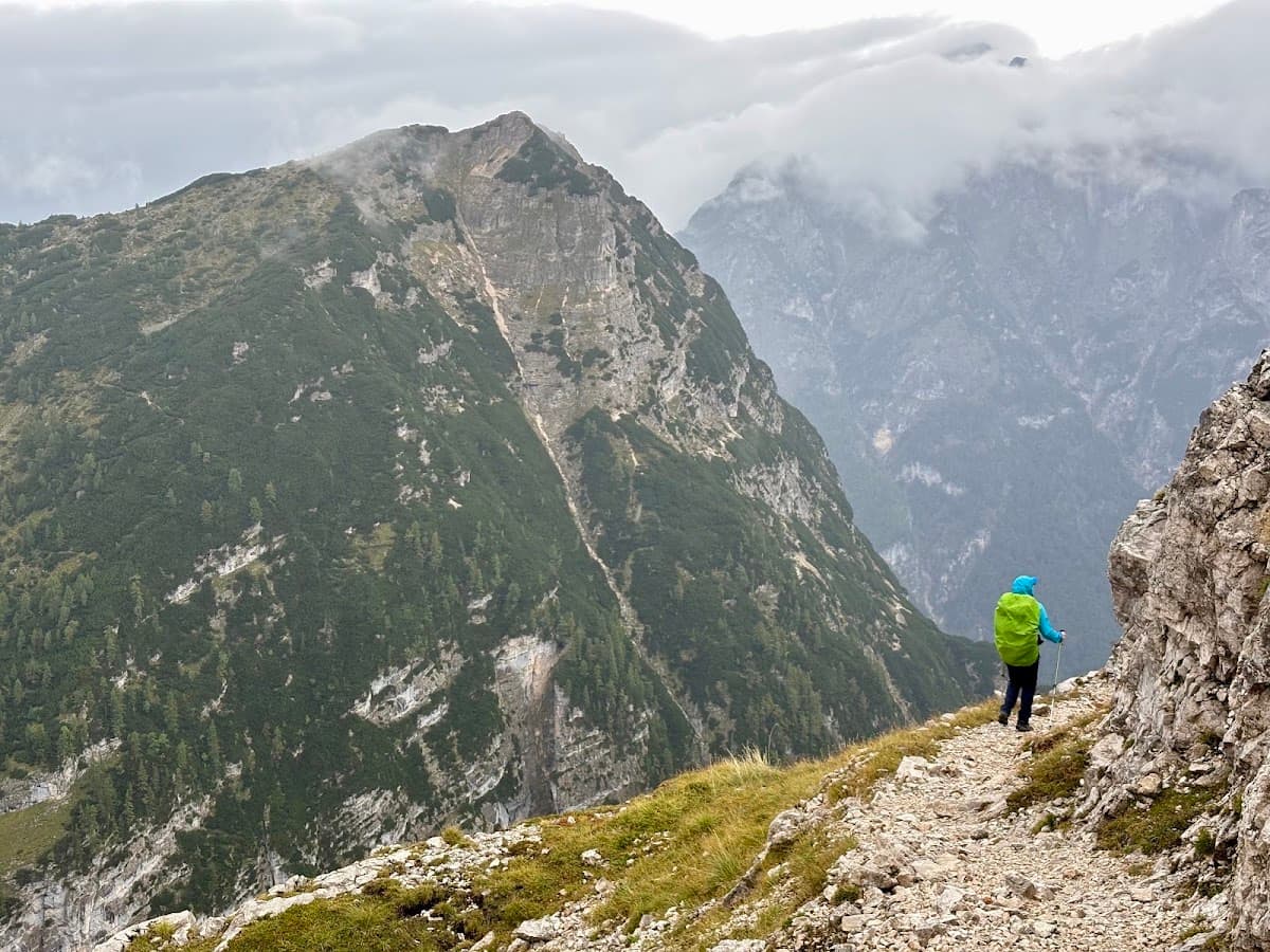 Hiker with green backpack on a rocky mountain trail overlooking alpine peaks